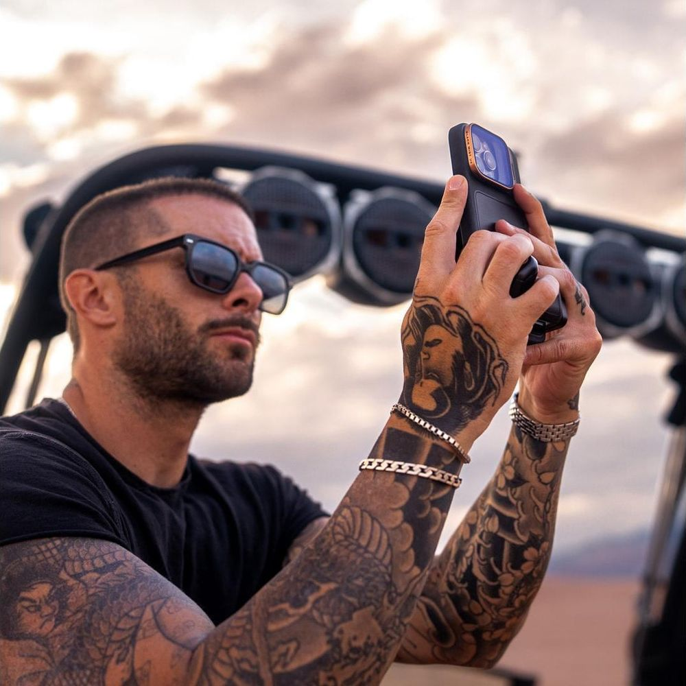 Mann mit Tattoos und Sonnenbrille macht ein Selfie mit seinem Handy.