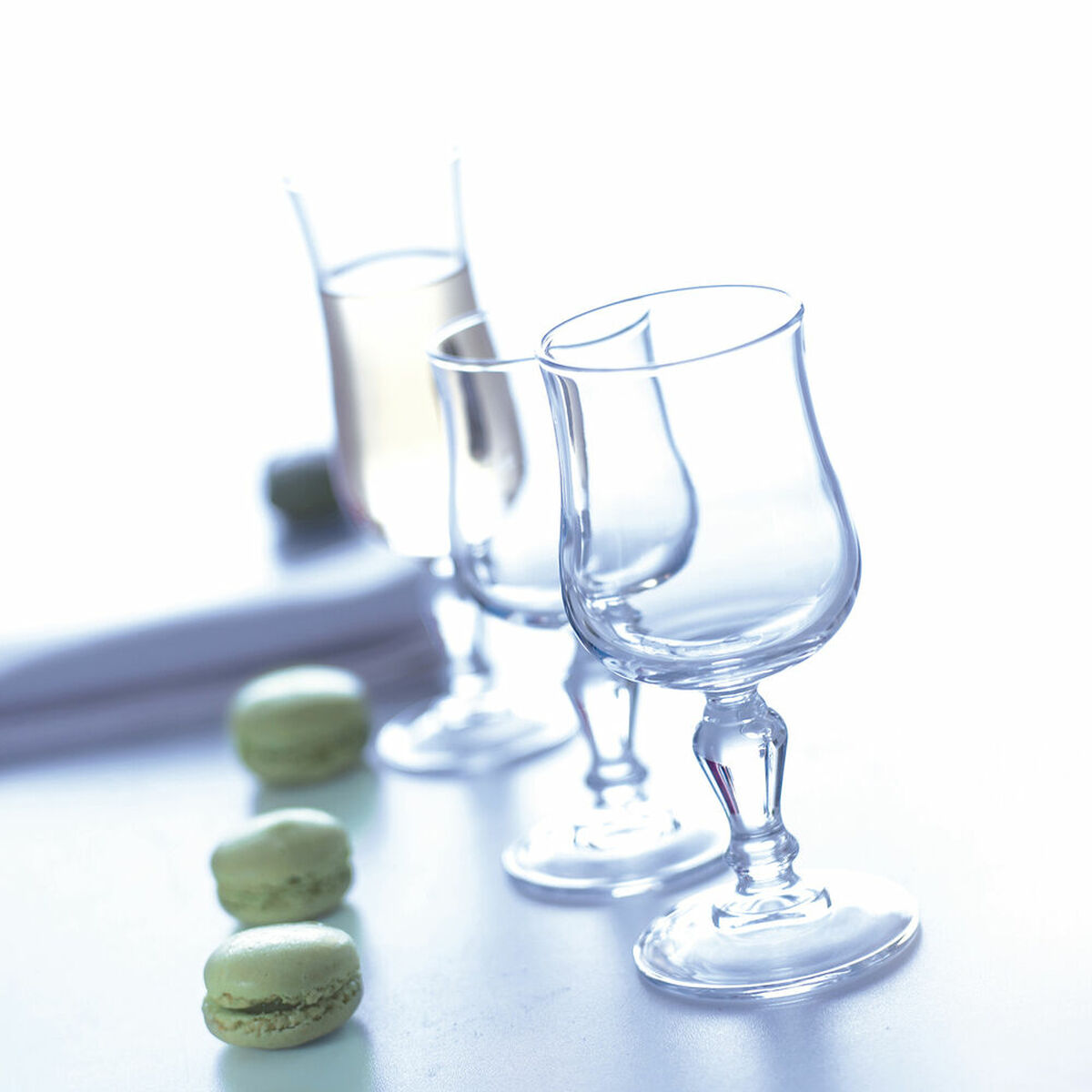 Drei grüne Macarons liegen auf einer weißen Oberfläche neben drei Weingläsern.