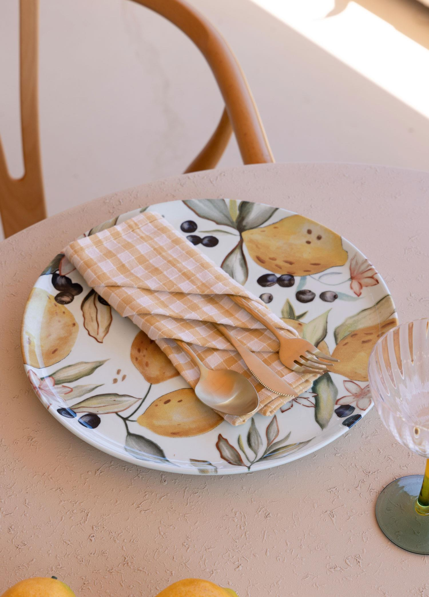 Masanın üzerinde limon ve zeytin desenli tabak, katlanmış peçete ve çatal-bıçak takımı.