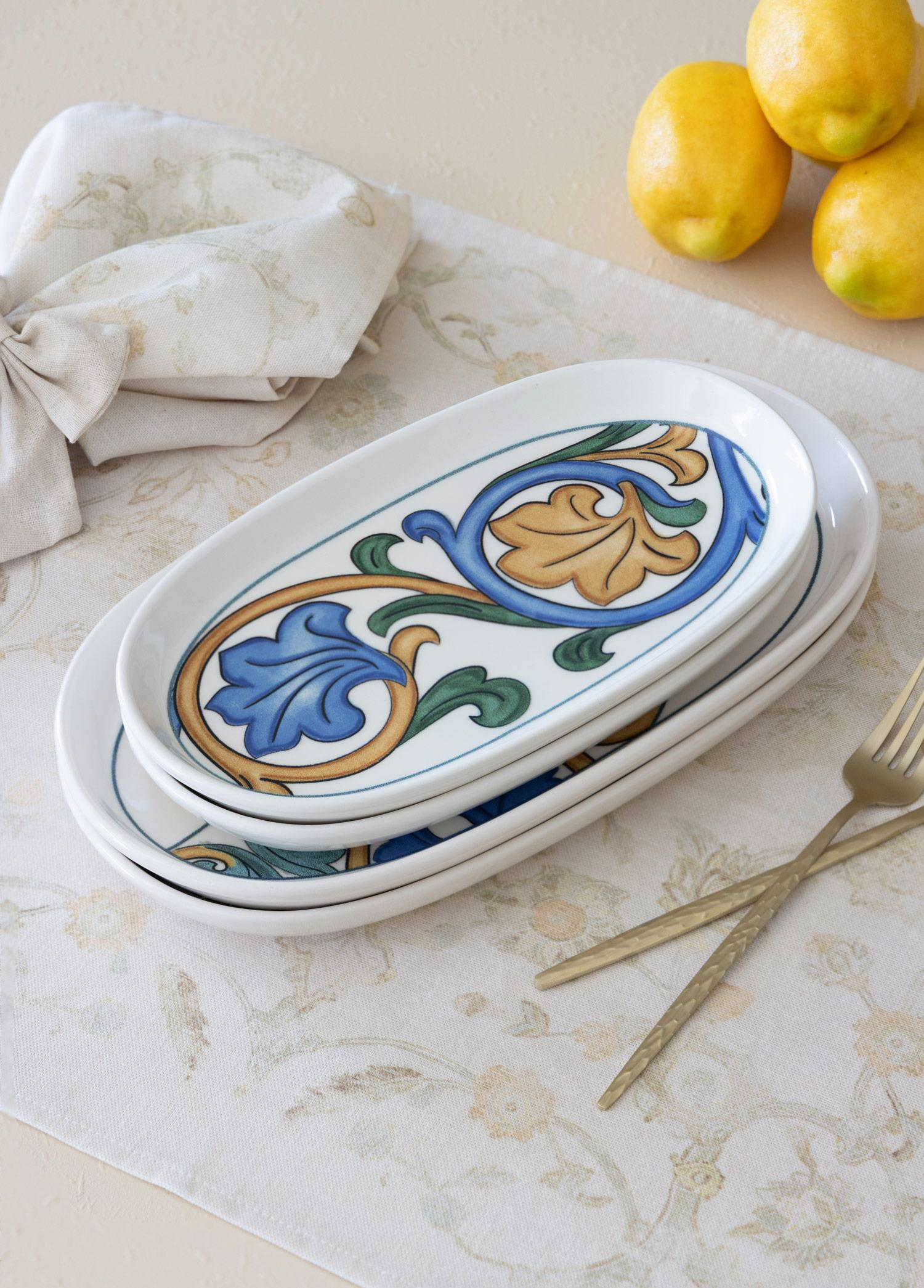 Mavi ve sarı çiçek desenli iki oval tabak, yanında limonlar ve çatallar.