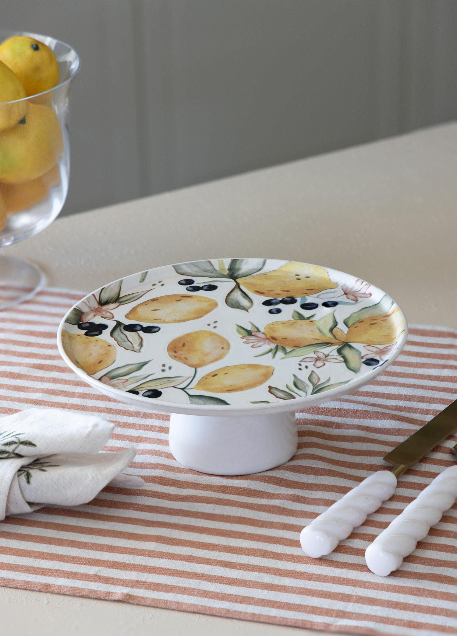 Limon ve zeytin desenli beyaz pasta standı çizgili masa örtüsünün üzerinde duruyor.