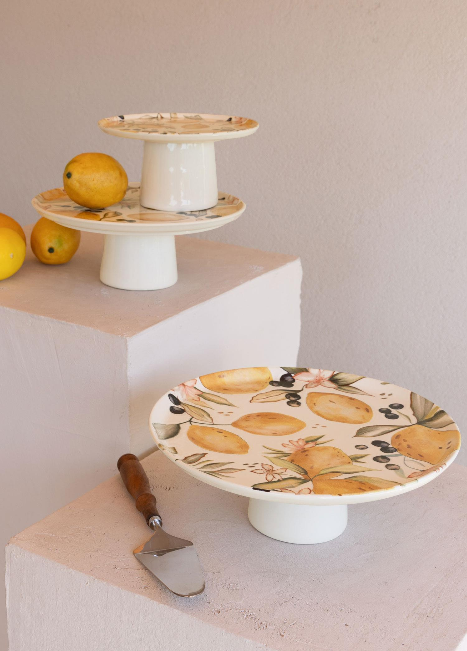 Limon desenli iki beyaz pasta standı, yanında limonlar ve pasta servis bıçağı.