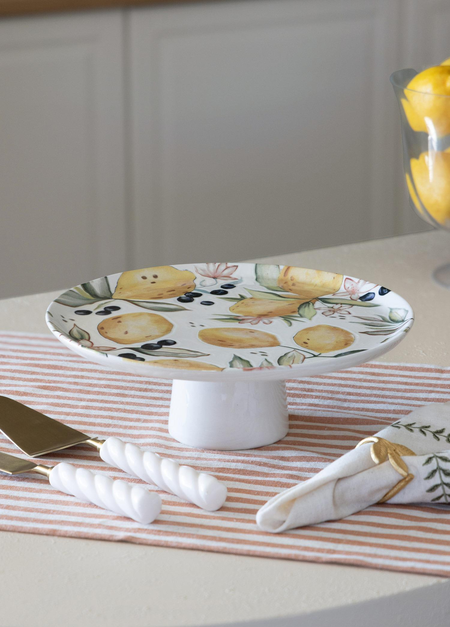 Limon desenli beyaz pasta standı, yanında servis gereçleri ve peçete.