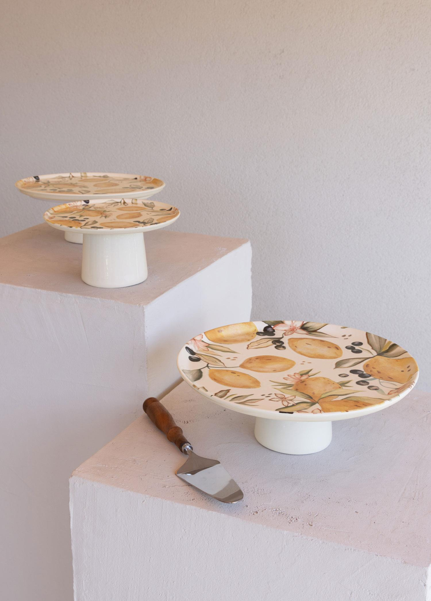 Limon ve çiçek desenli üç beyaz pasta standı, biri pasta servis spatulası.