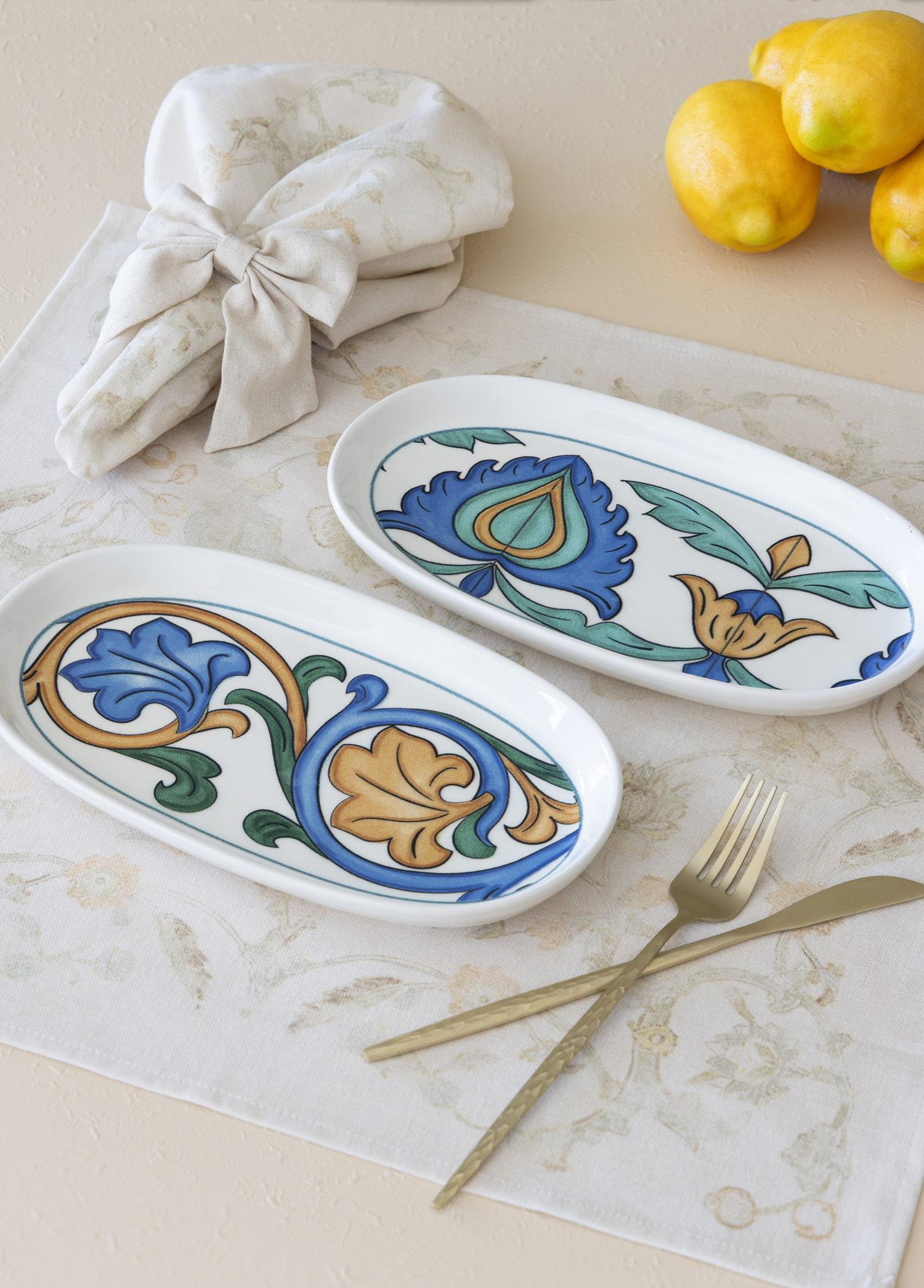 Mavi ve altın rengi çiçek desenli iki oval tabak masa örtüsünde duruyor.