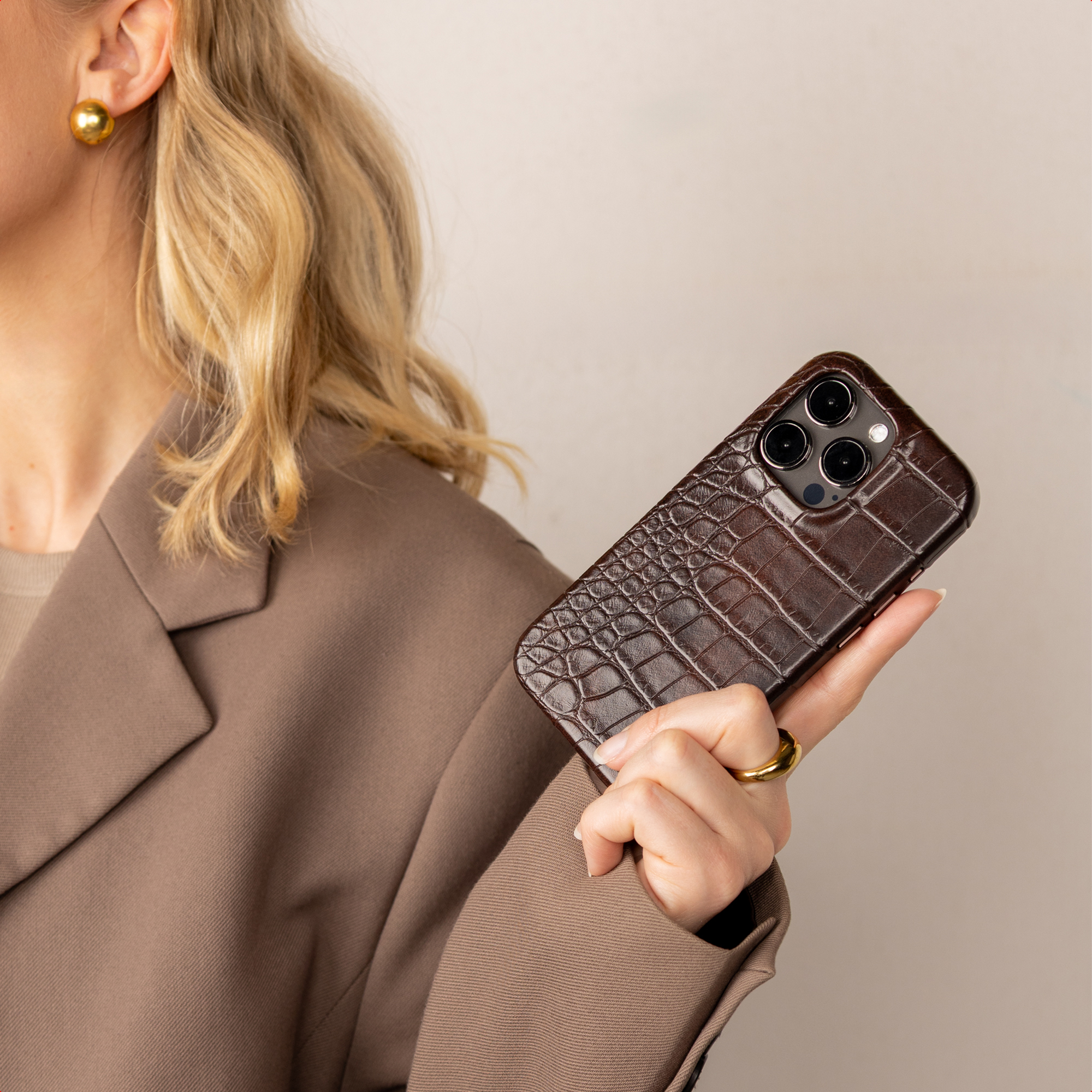 Een blonde vrouw houdt een bruine telefoonhoes met krokodillenprint vast.