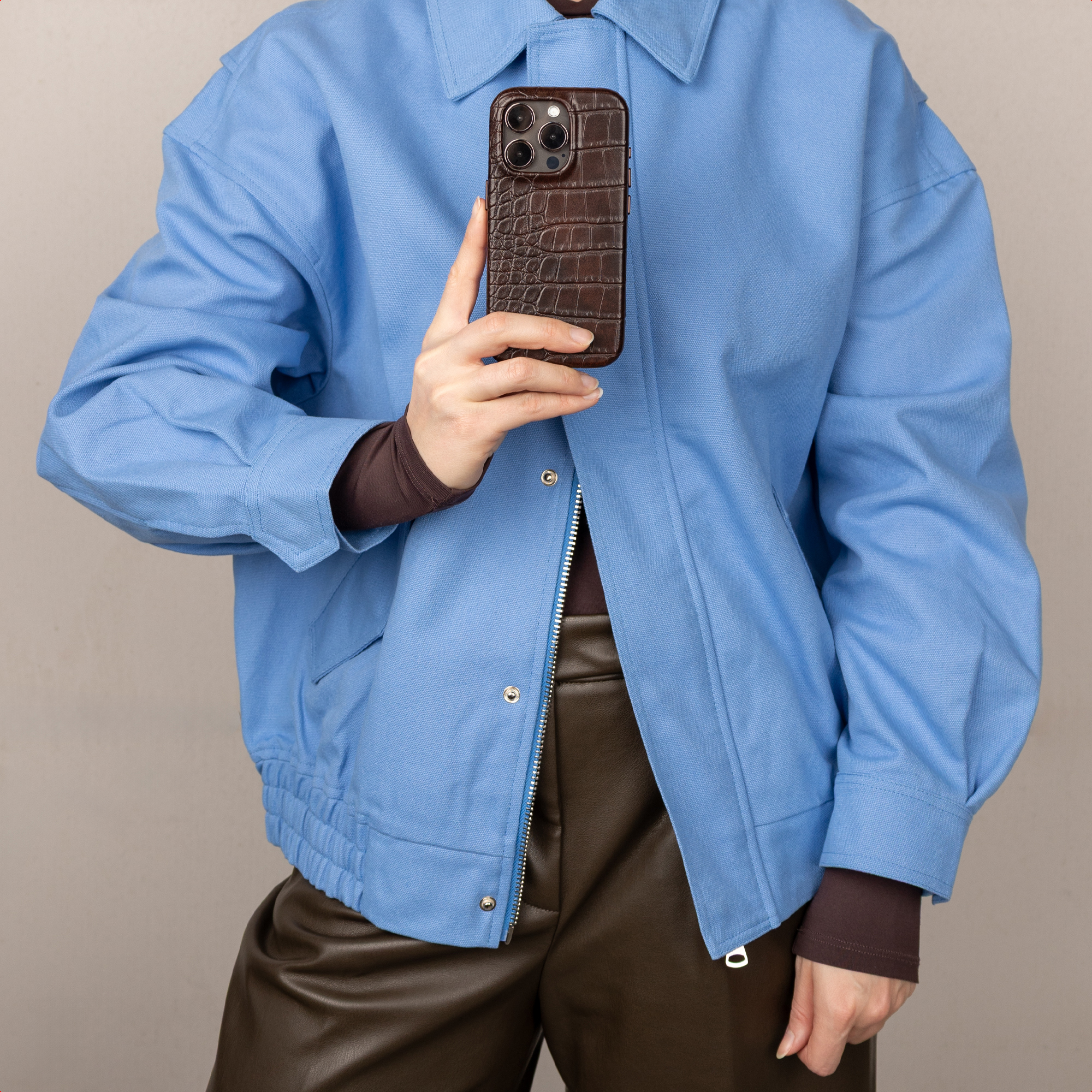 Een persoon in een blauw jasje houdt een bruine telefoonhoes vast.