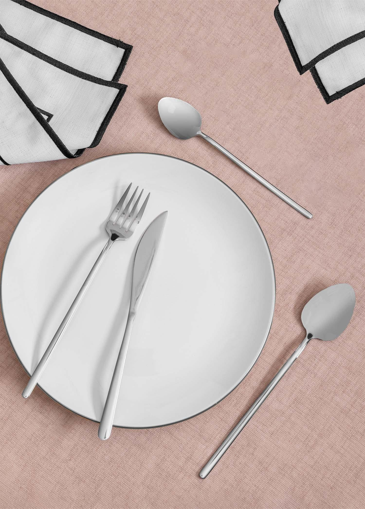 Pembe masa örtüsü üzerinde çatal bıçak ve peçeteli beyaz tabak.