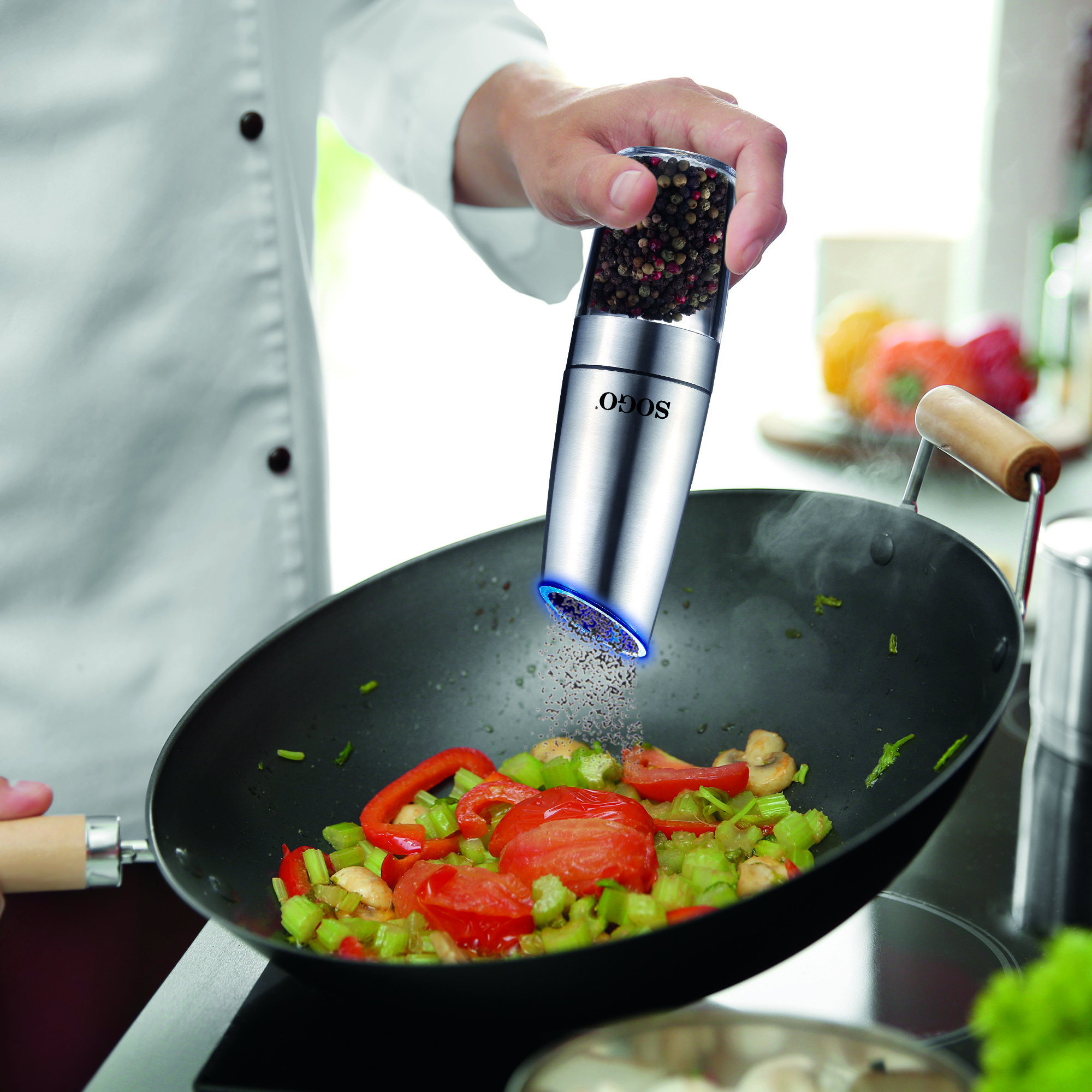 Uno chef condisce verdure in un wok con un macinapepe elettrico.