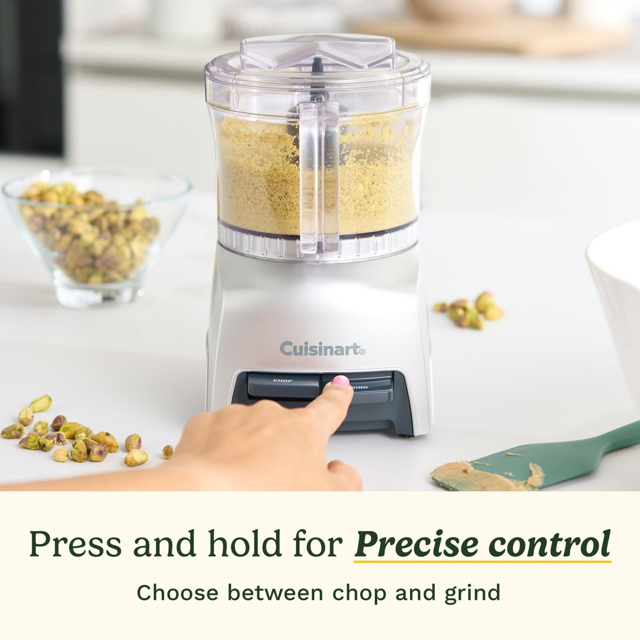 Robot da cucina compatto con pistacchi tritati e una mano che preme un pulsante.