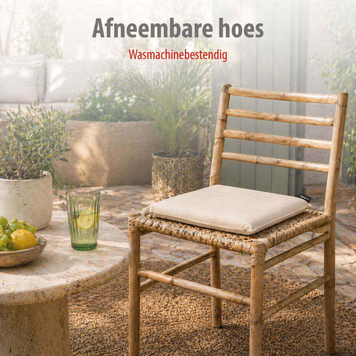 A bamboo chair with a cream cushion sits on gravel. Beside it a table with fruit and a glass.
