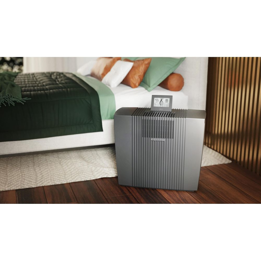 Un purificateur d'air gris à côté d'un lit avec une literie verte.