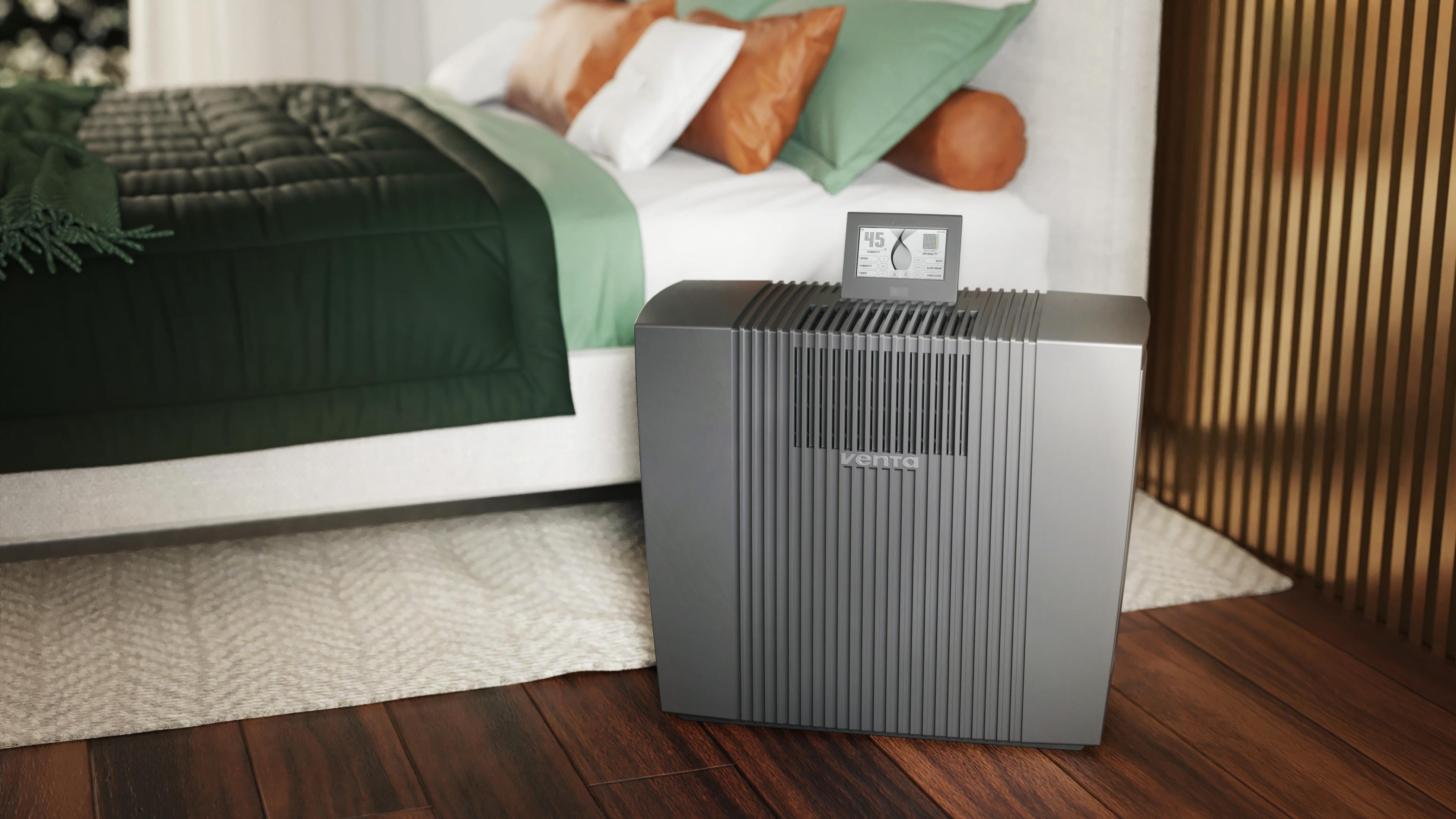 Un purificateur d'air gris à côté d'un lit avec une literie verte.