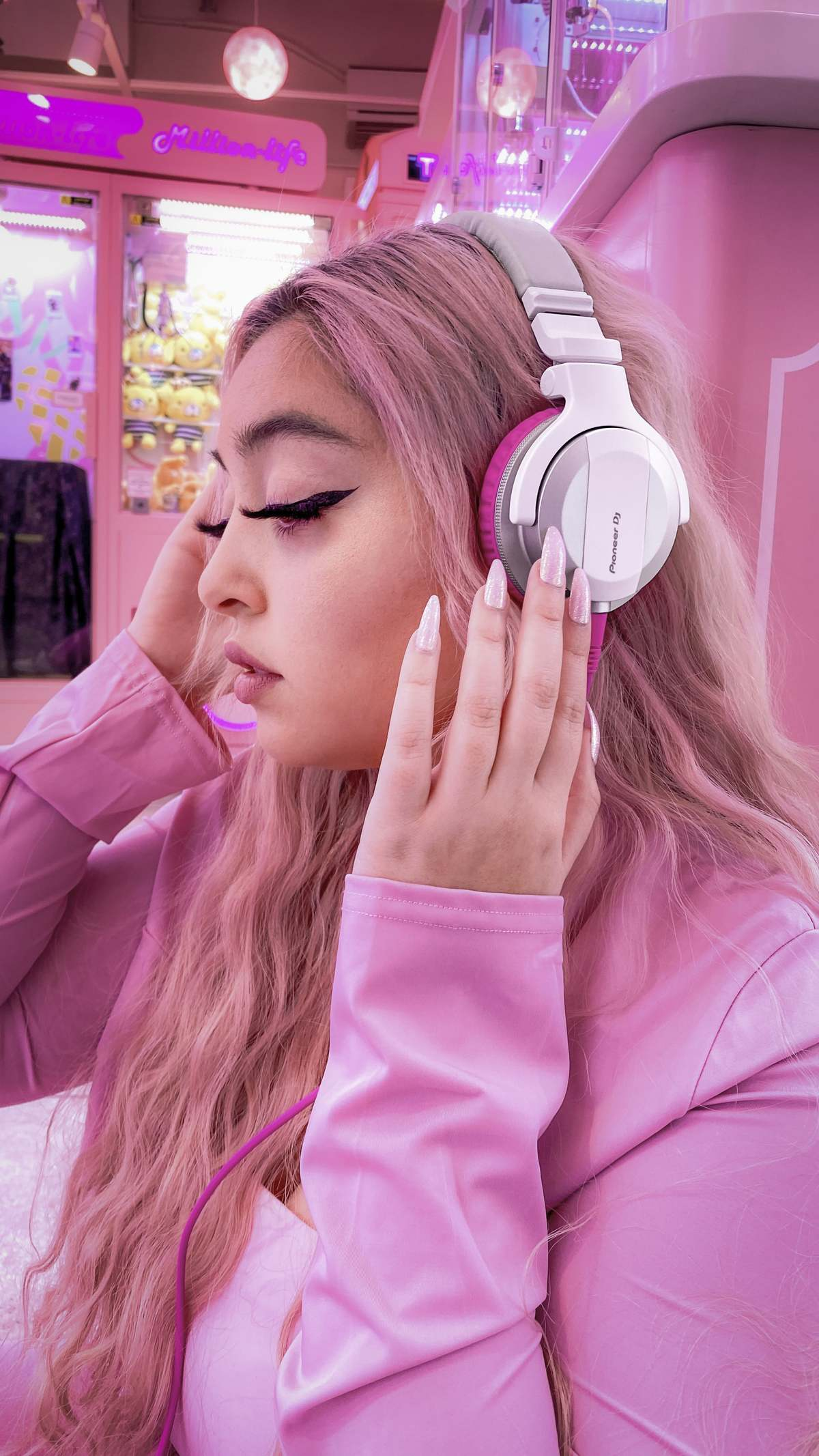 Młoda kobieta z różowymi włosami słucha muzyki przez białe słuchawki.