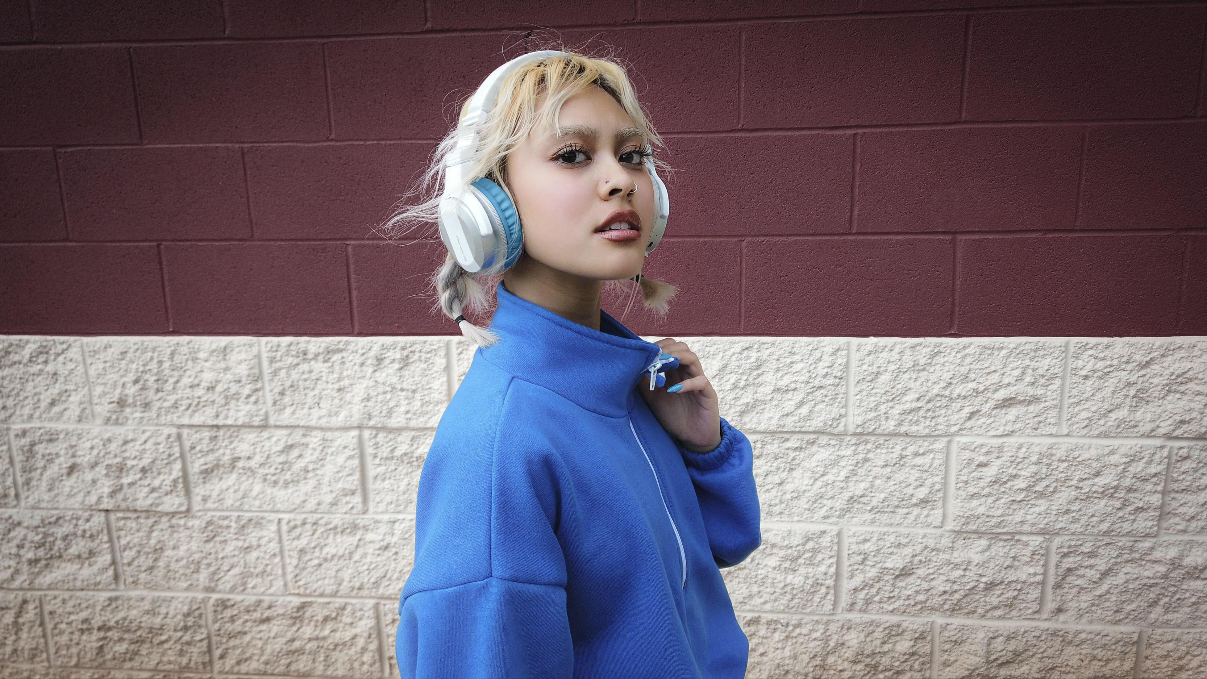 Kobieta w blond włosach ze słuchawkami stoi przed ceglanym murem.