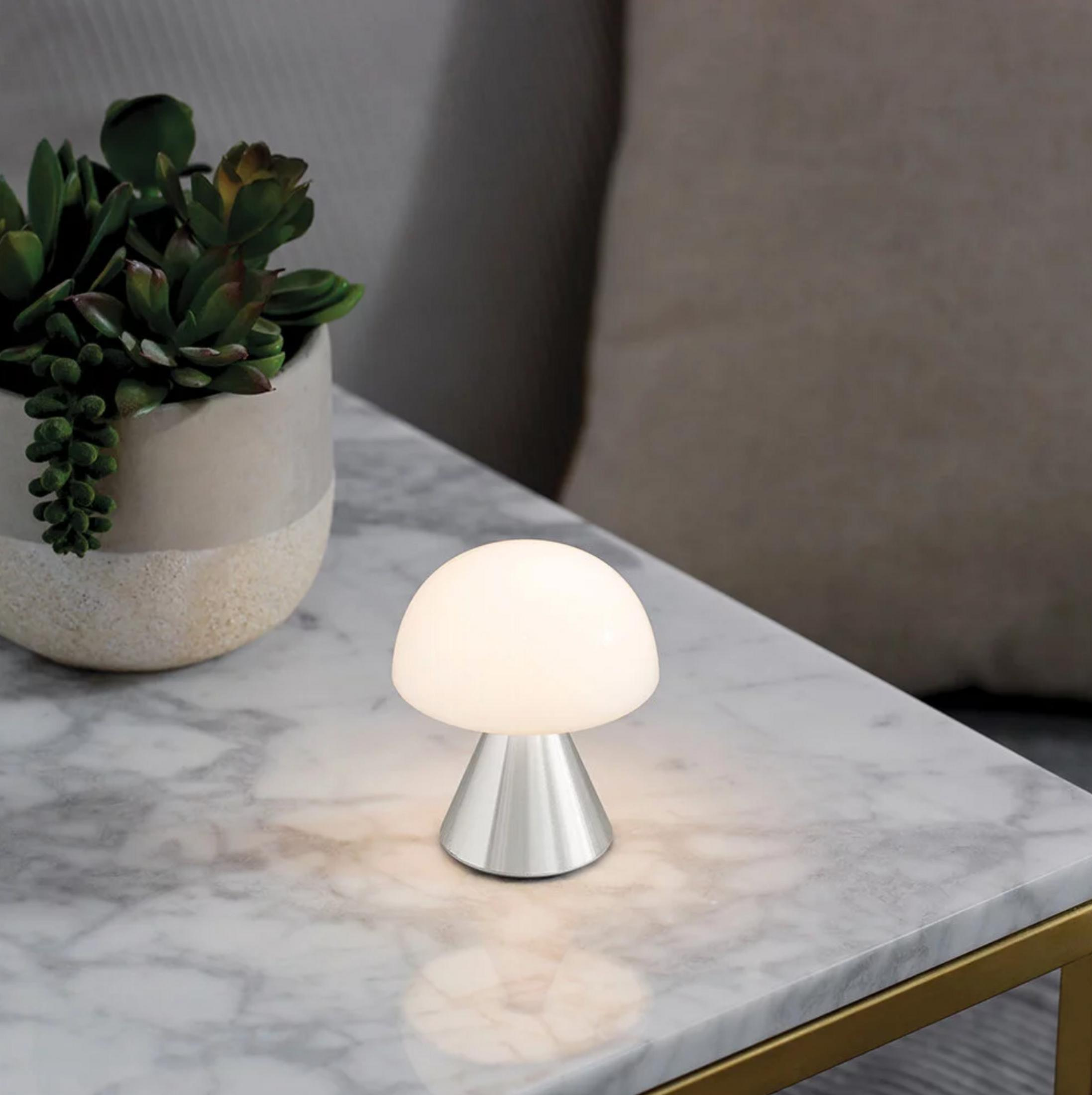 Eine Pilzlampe leuchtet auf einem Marmortisch neben einer Topfpflanze.