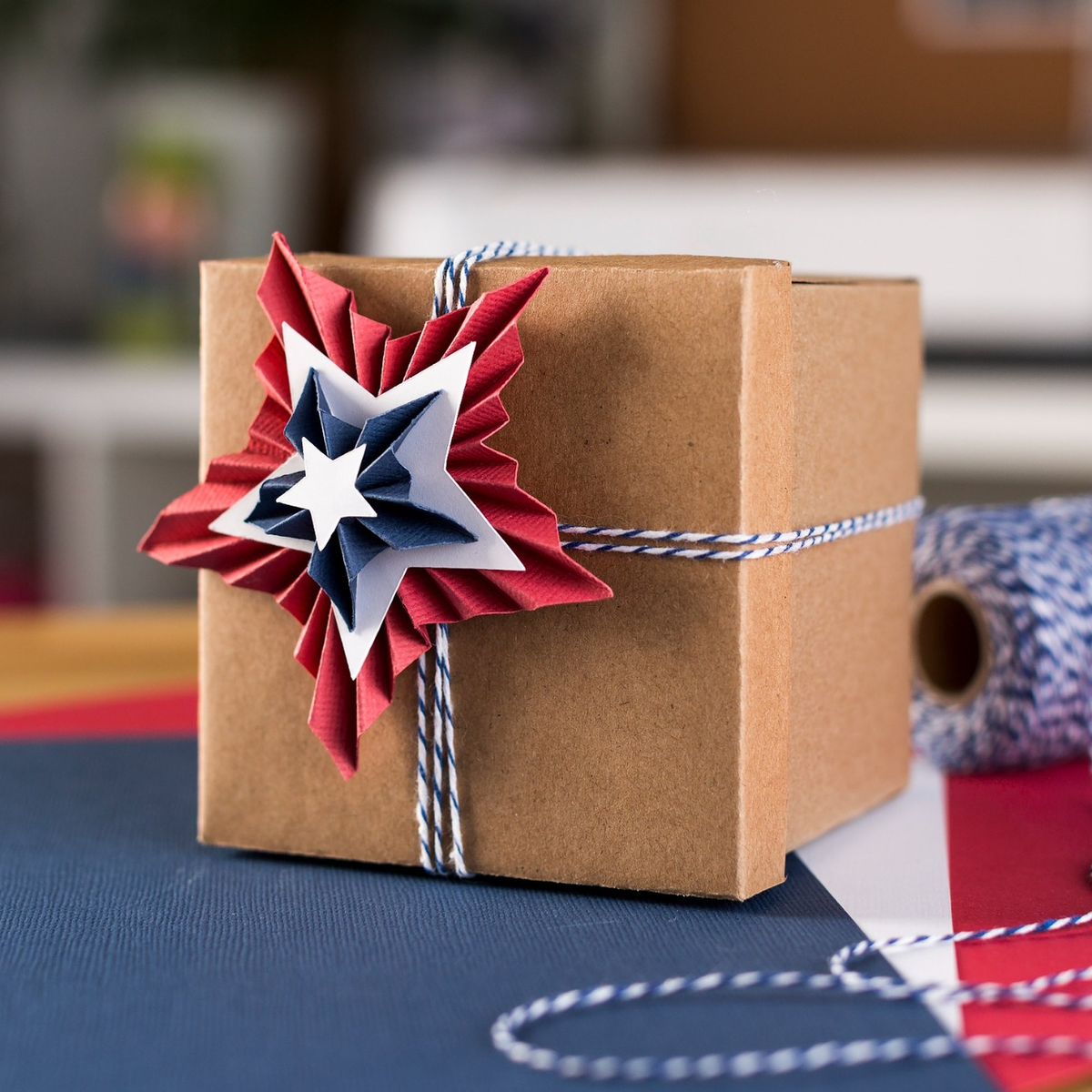 Ein braunes Geschenkpaket mit roter, weißer und blauer Sternendekoration, gebunden mit einer Schnur.