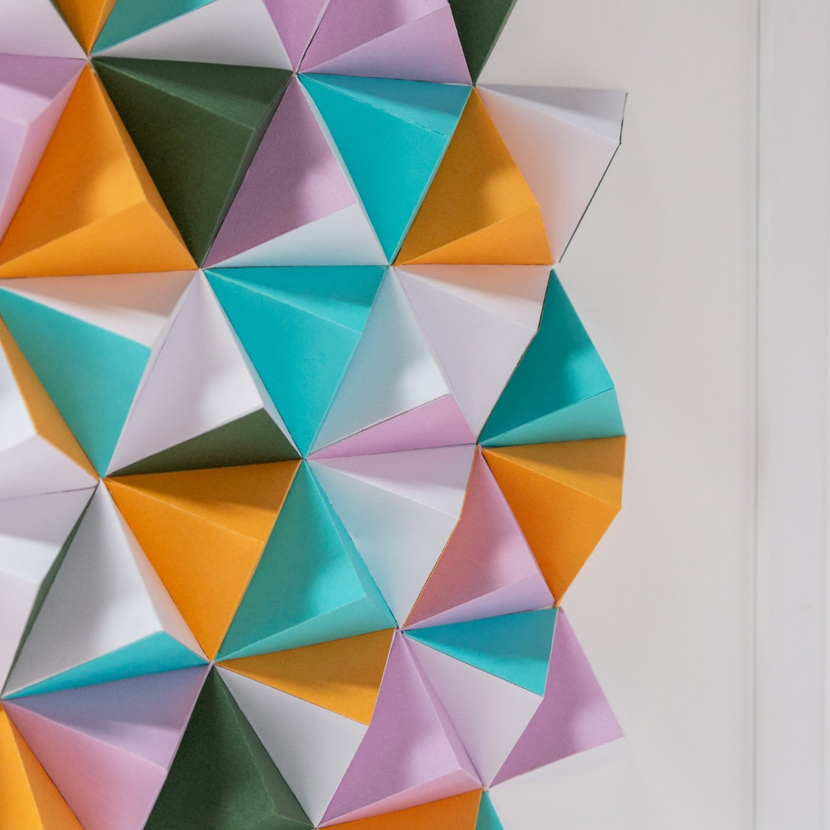 Geometrisches Origami-Muster aus dreieckigen Papierstücken in Blau, Orange, Lila und Grün.