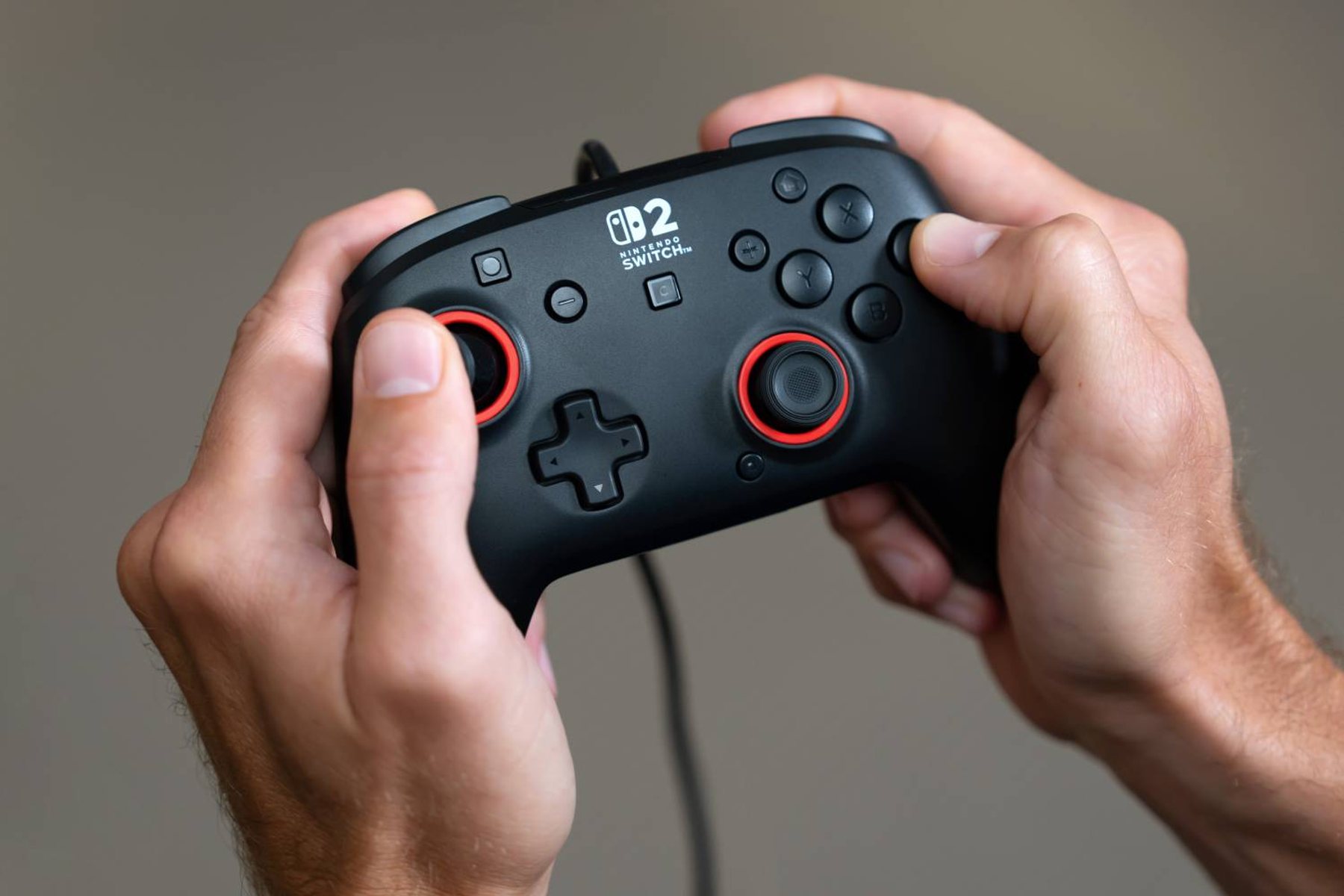 Schwarzer Nintendo Switch Controller mit roten Akzenten, gehalten von zwei Händen.