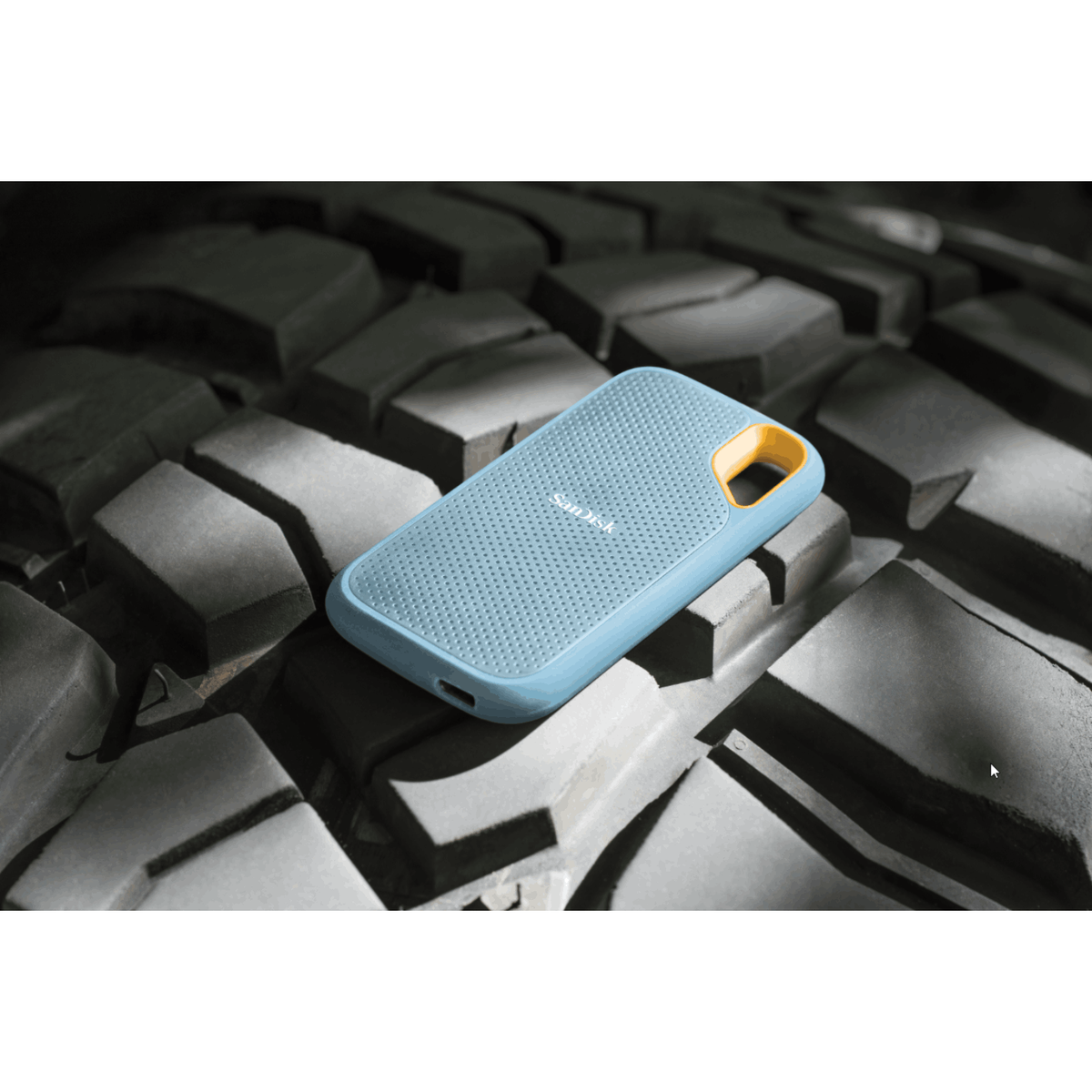 Un'unità SanDisk blu chiaro con anello giallo poggia su0scanalature di pneumatici grezze.
