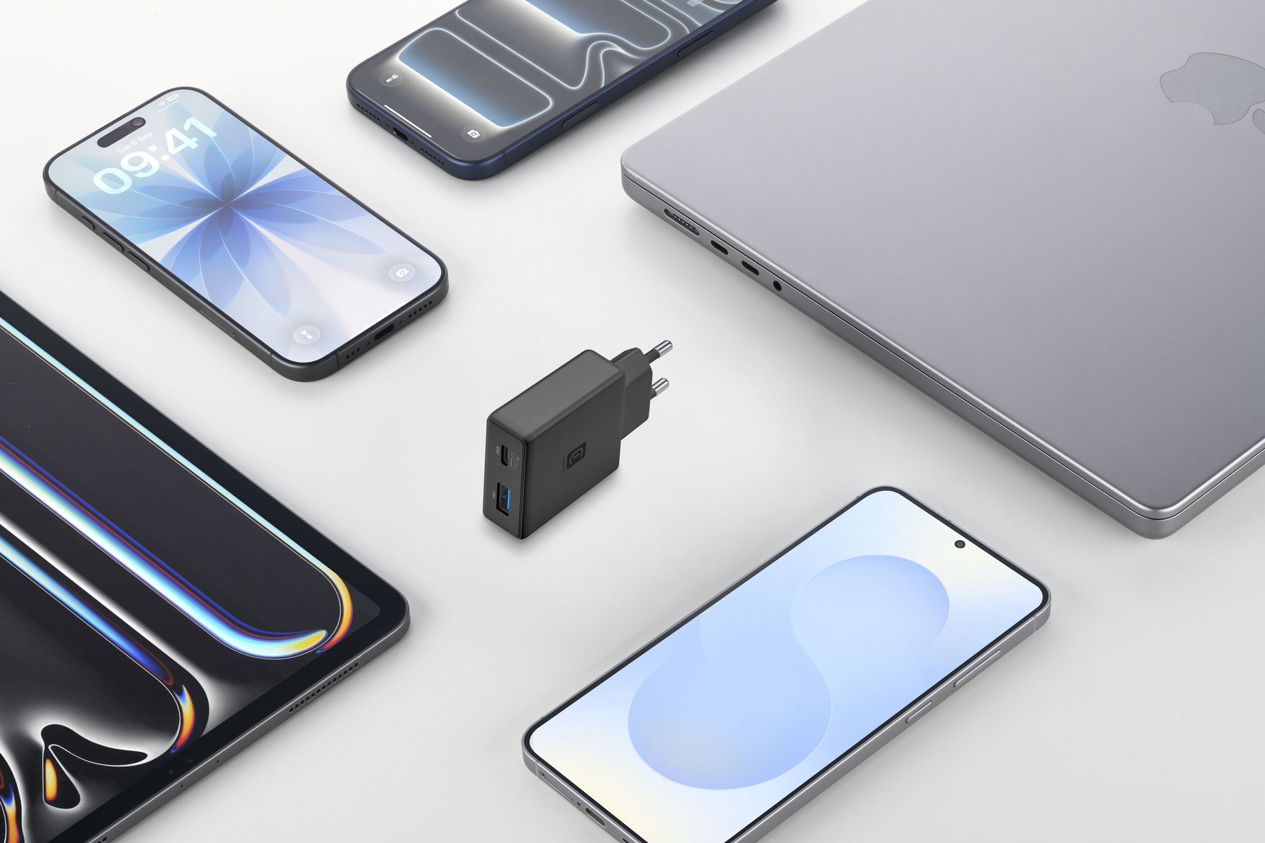 Ein schwarzer Reiseadapter mit zwei USB-Anschlüssen liegt zwischen Smartphones, einem Laptop und einem Tablet.