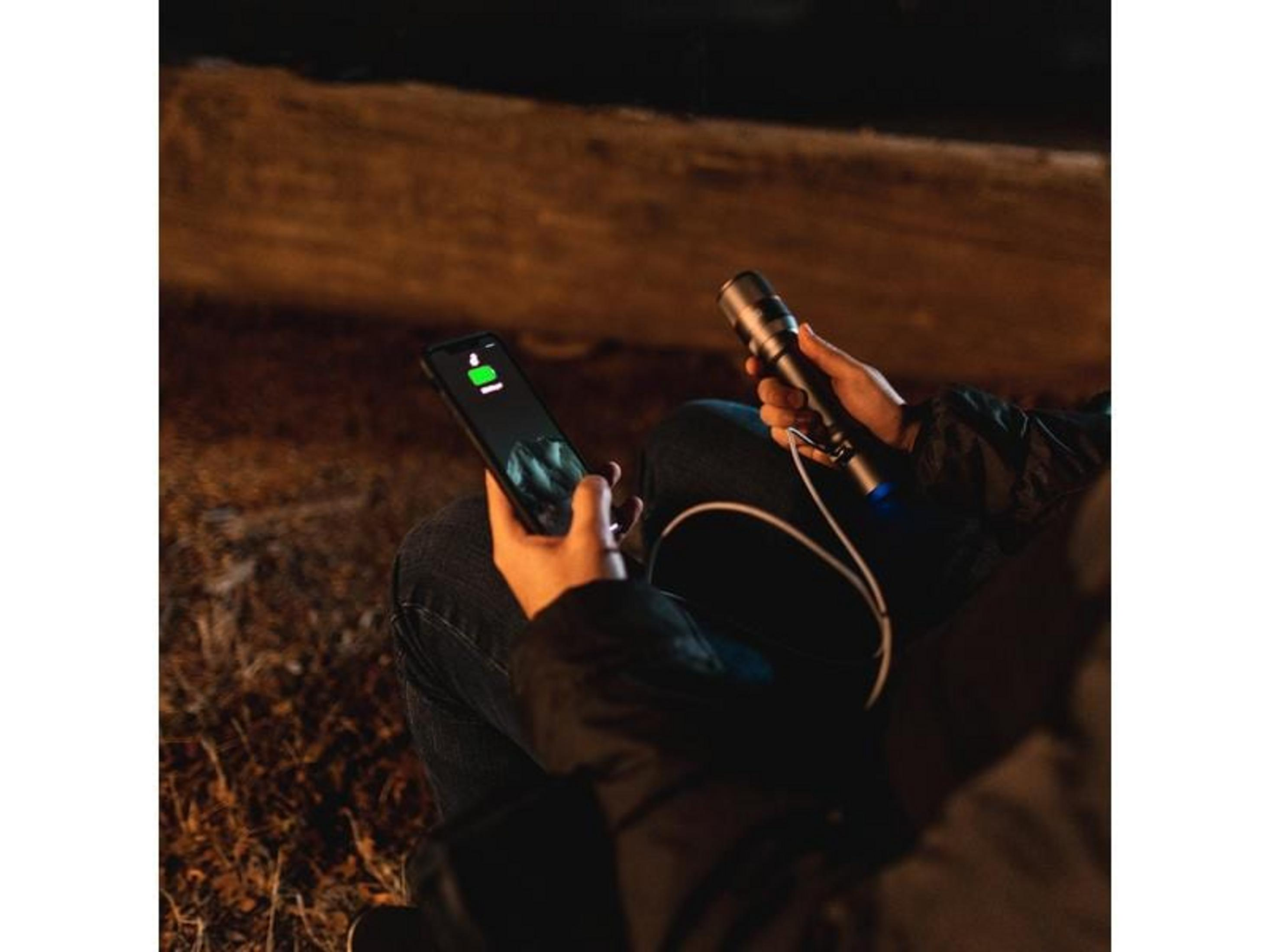 Eine Person hält ein Smartphone und eine Taschenlampe im Dunkeln.