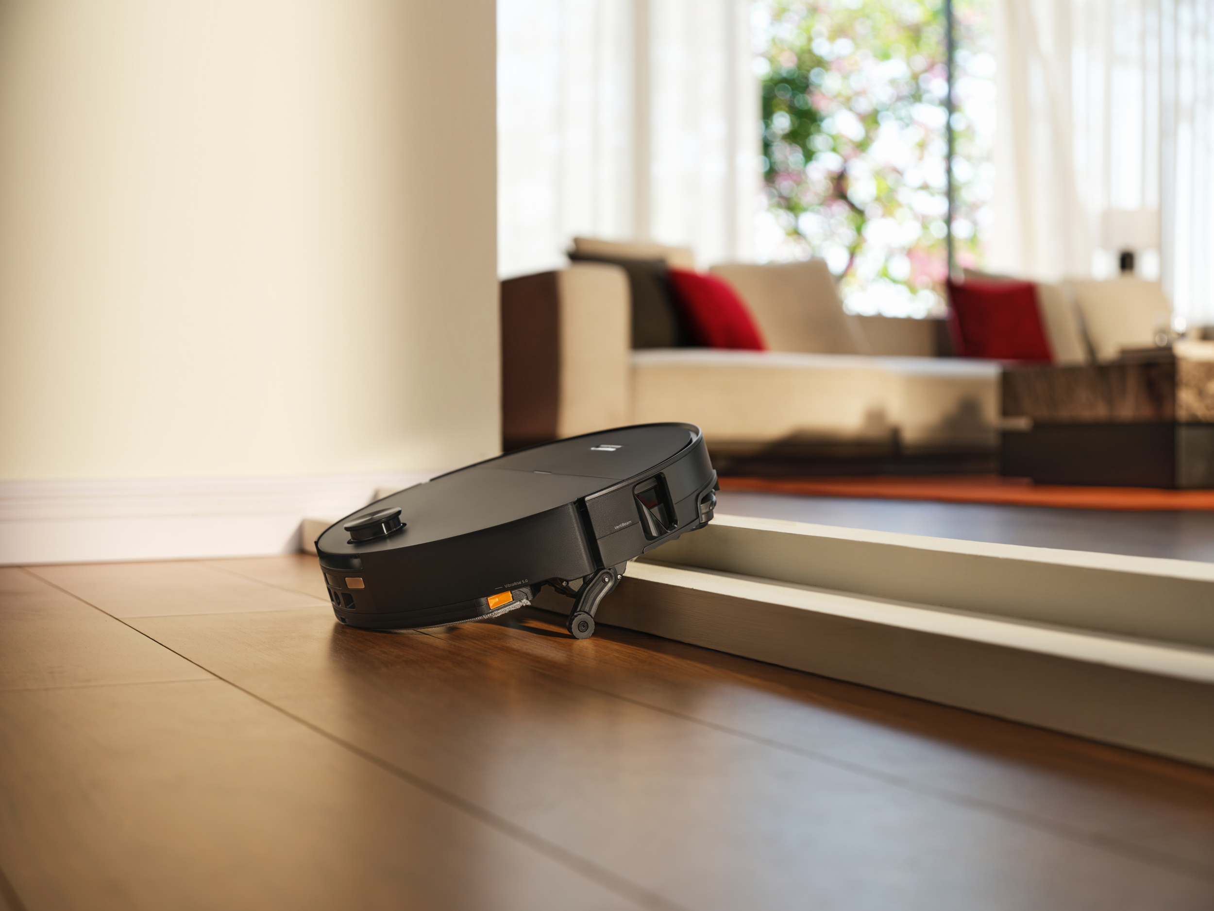 Un robot aspirateur noir se déplace sur un parquet le long d'une plinthe.