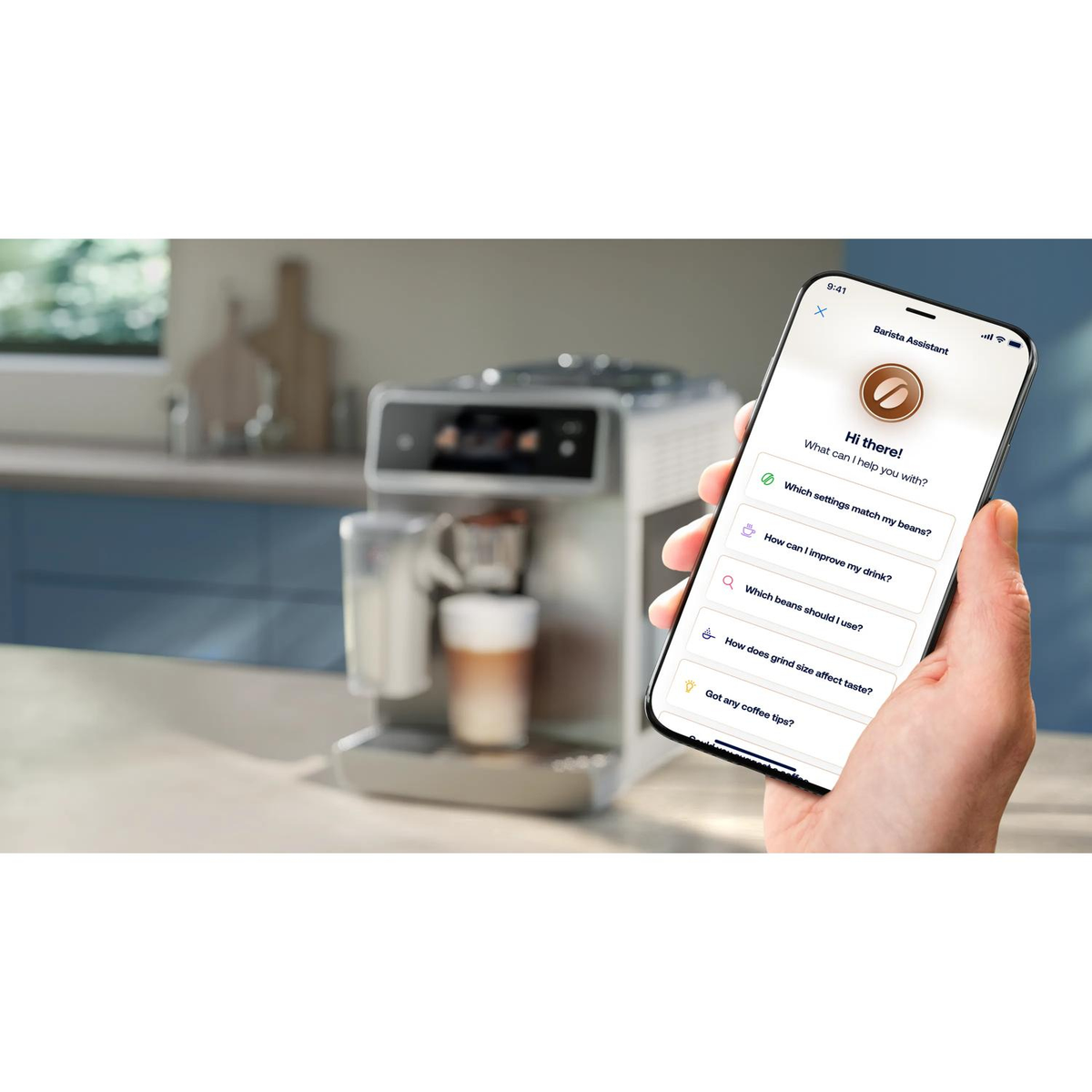 Eine Hand hält ein Smartphone mit Kaffeemaschinen-App vor einer Kaffeemaschine.