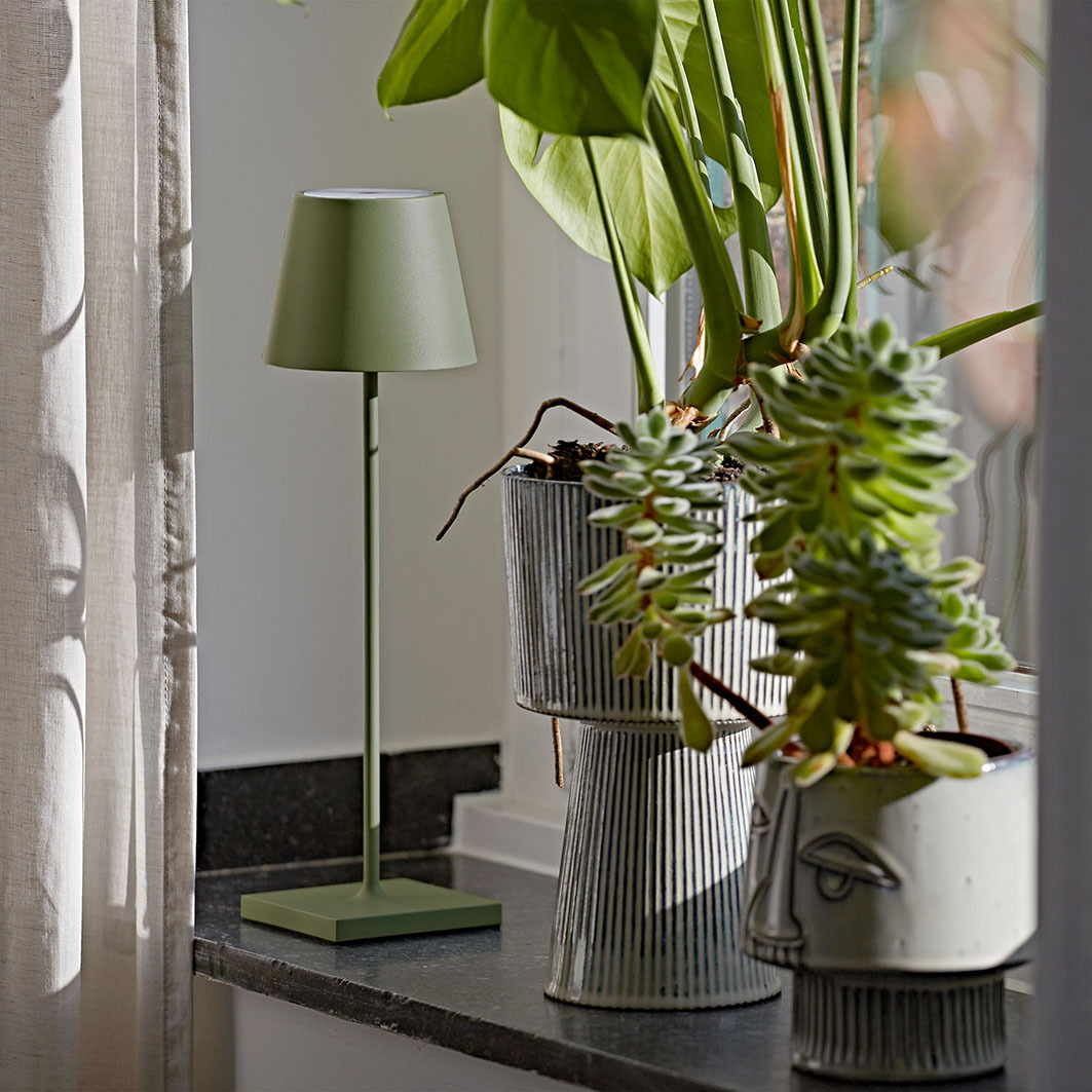 Grüne Lampe neben Pflanzen auf Fensterbank, Vorhang daneben.