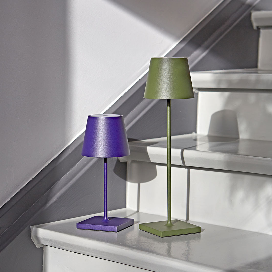 Zwei moderne schnurlose Lampen, eine lila, eine grüne, stehen auf einer weißen Treppe mit Schatten.