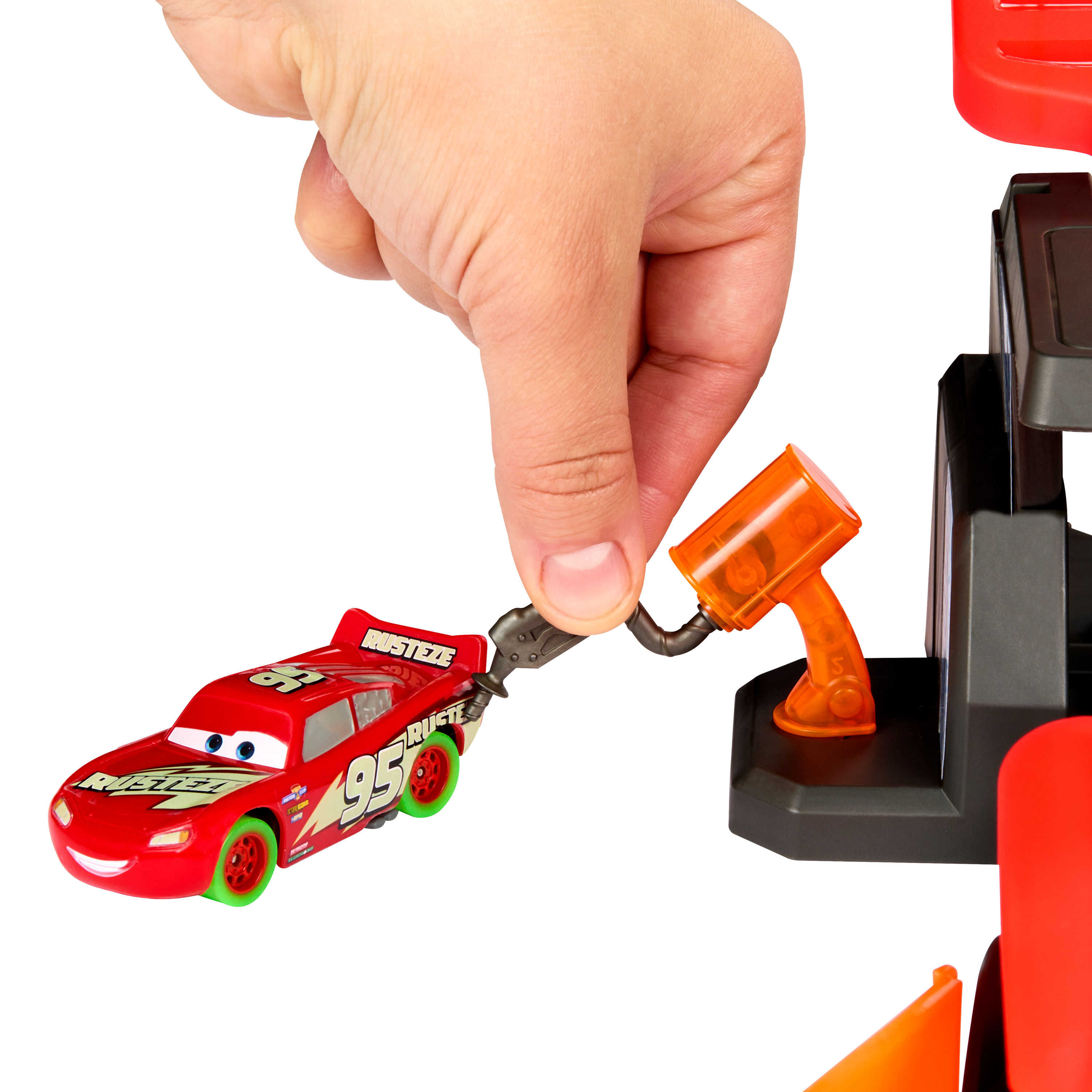 Ein Mann steckt Lightning McQueen in eine Tankpistole an einer roten und grauen Tankstelle.