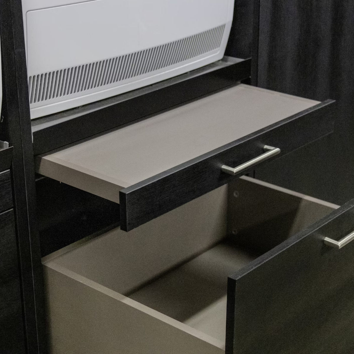 Ein weißes Gerät sitzt auf einem dunkelbraunen Holzschrank mit zwei offenen Schubladen.
