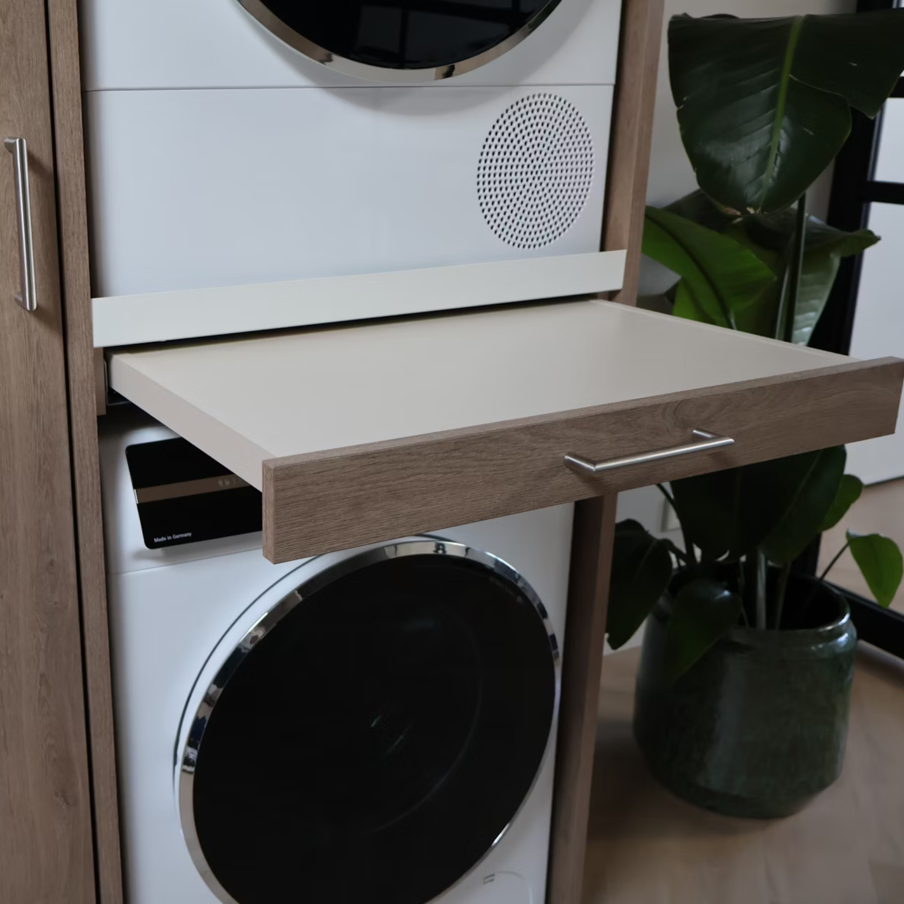 Weiße Waschmaschine mit ausziehbarem Tisch und Holzakzenten, daneben eine Pflanze.