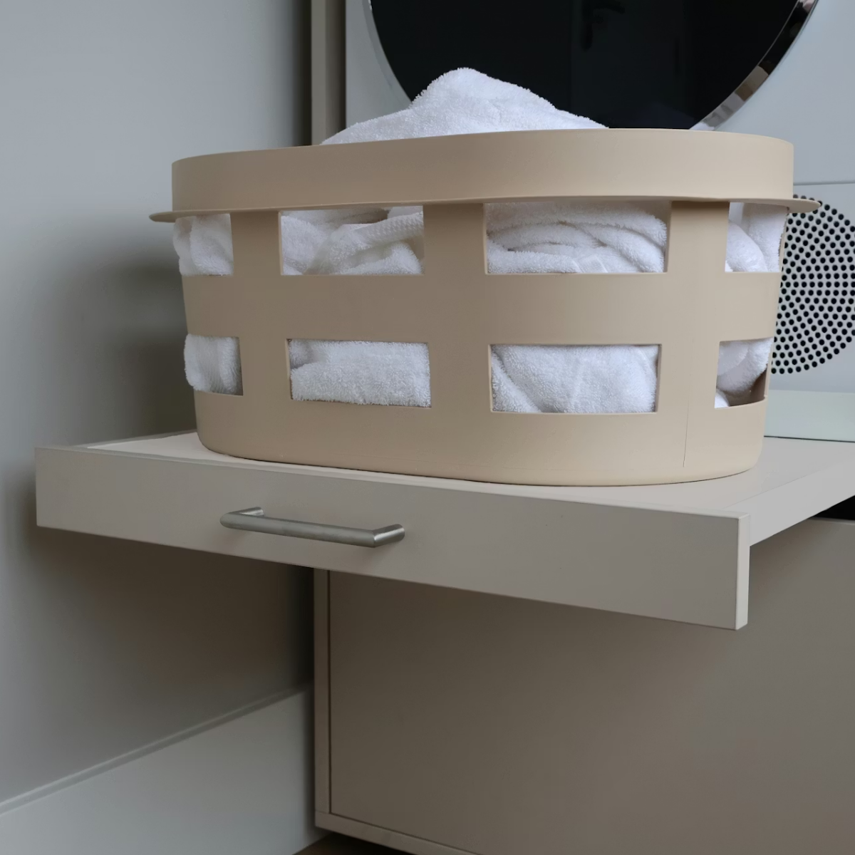 Beige Wäschekorb mit weißen Handtüchern auf einem Schubladenschrank.