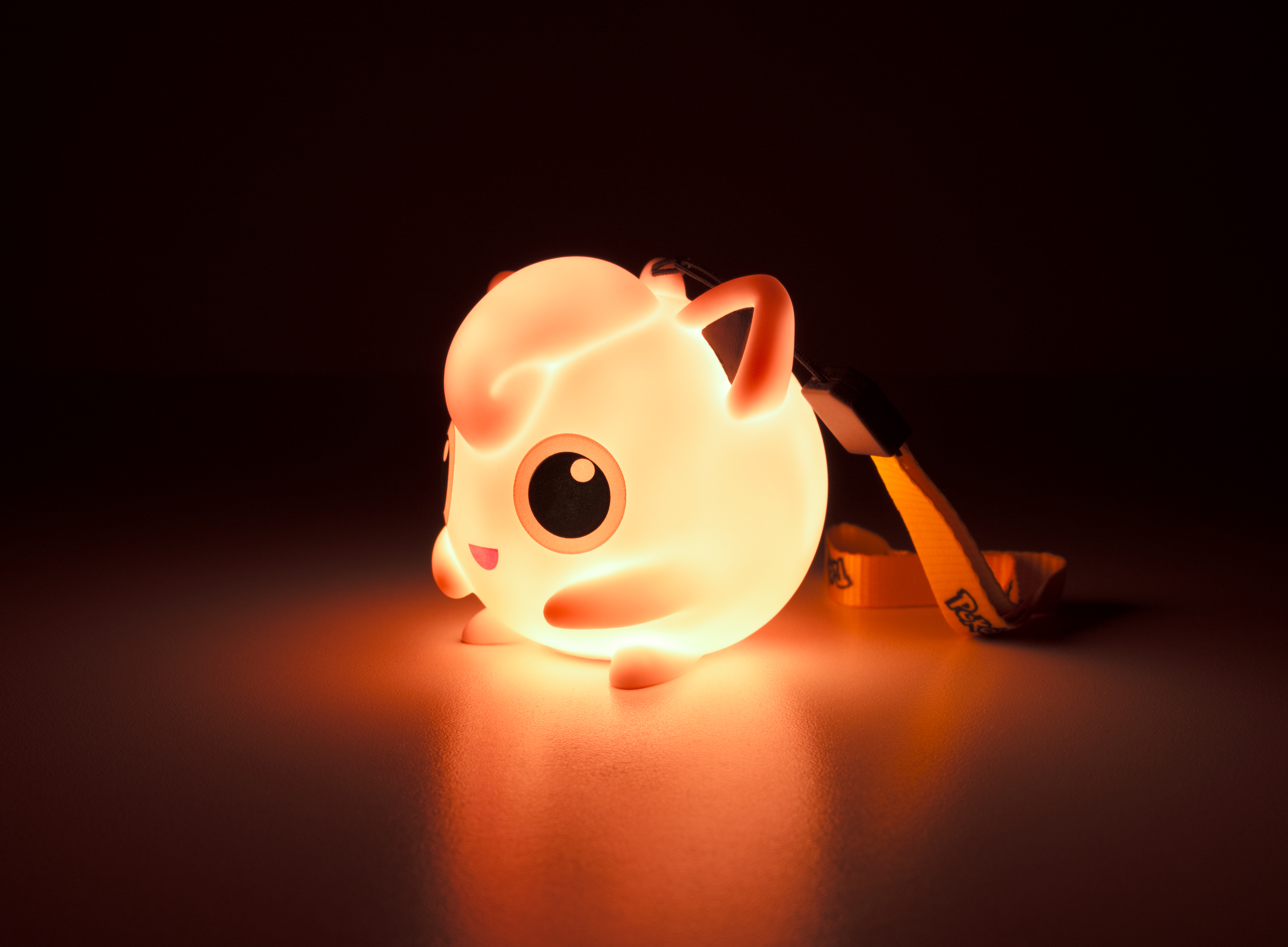 Una figura brillante de Jigglypuff con un cordón sobre fondo oscuro.