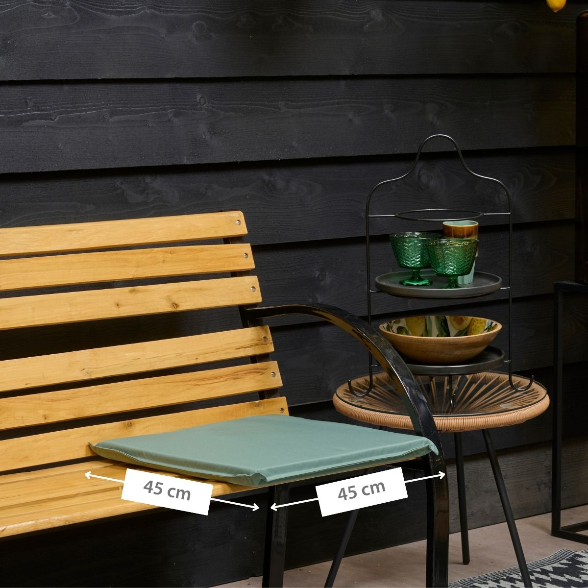 A wooden bench with a green cushion, next to it a shelf with glasses and bowls.