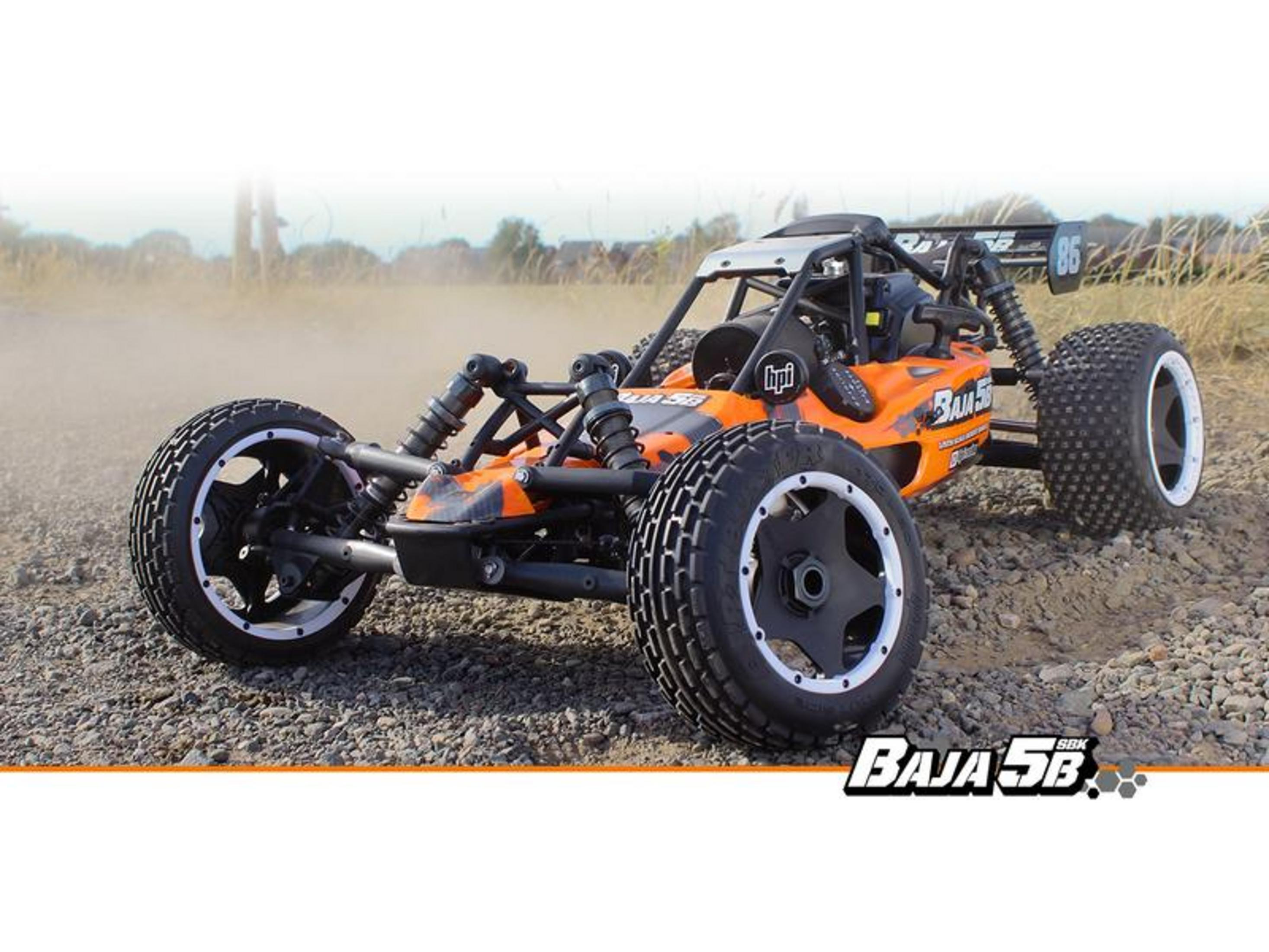 Un buggy naranja a control remoto se sienta sobre grava con un fondo polvoriento.