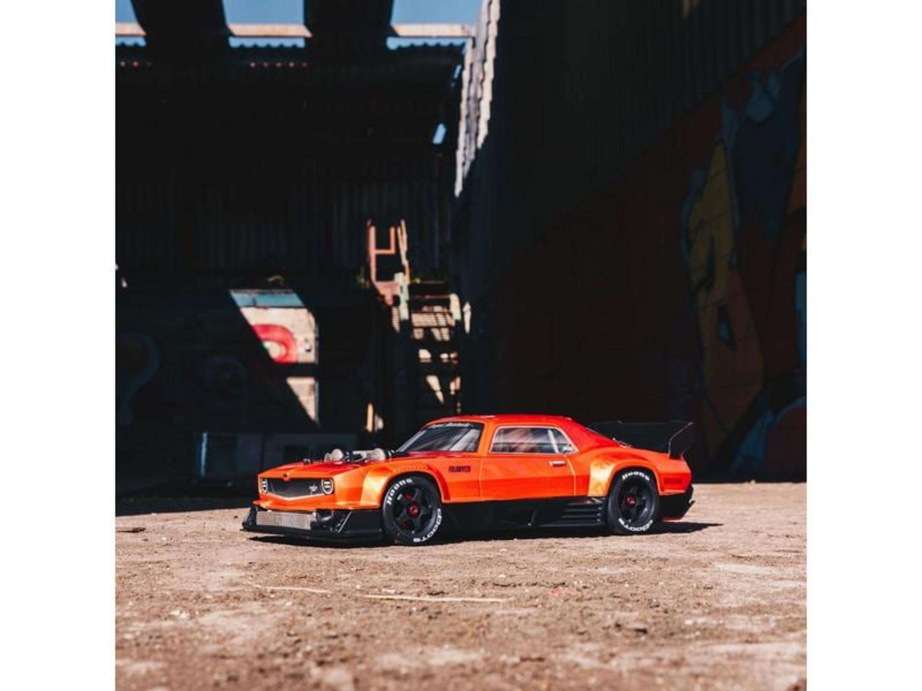 Un coche de carreras RC naranja brillante con alerón negro sobre grava.