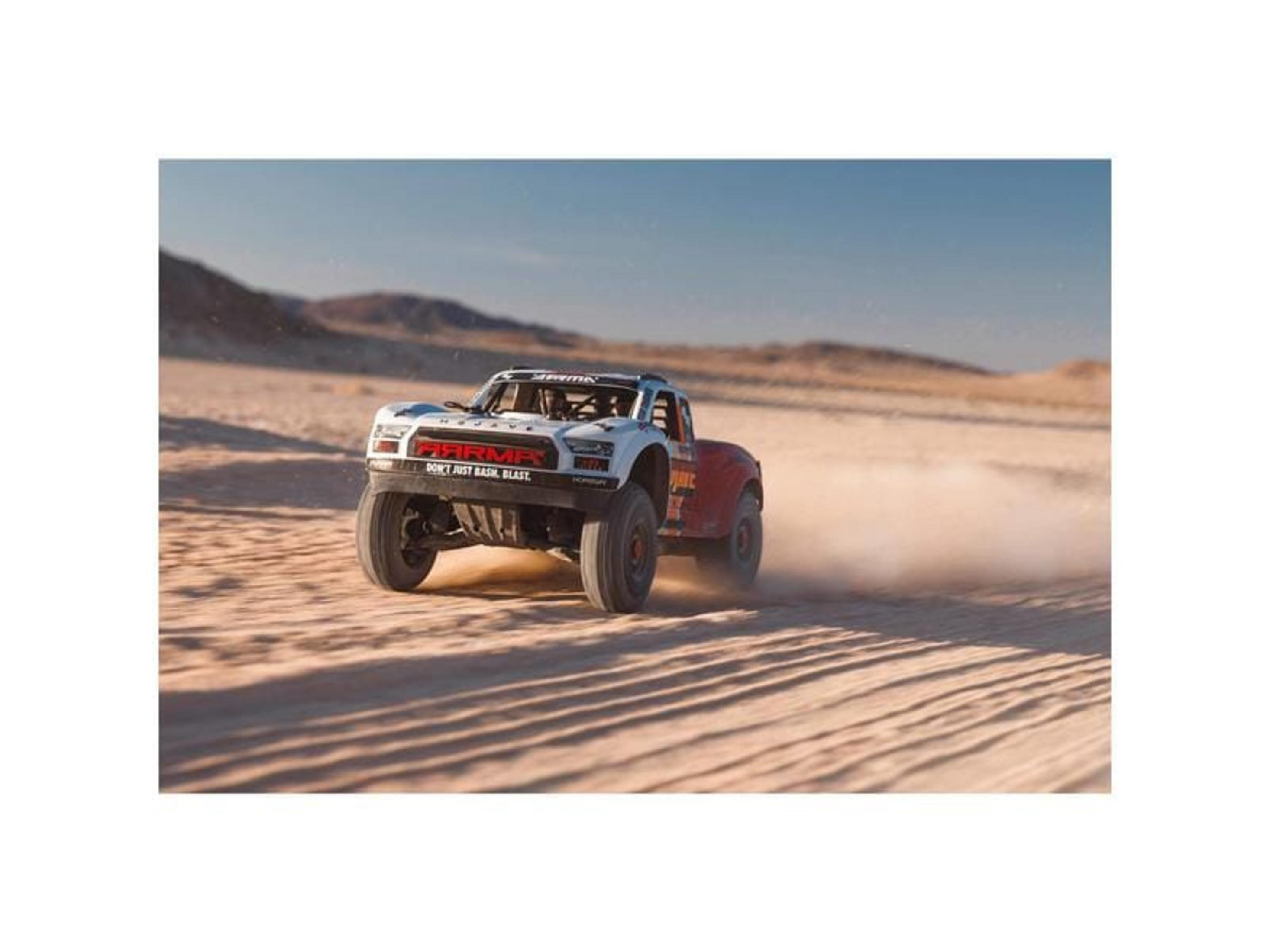 Ein weiß-roter RC-Truck fährt durch Sand und wirbelt Staub auf.