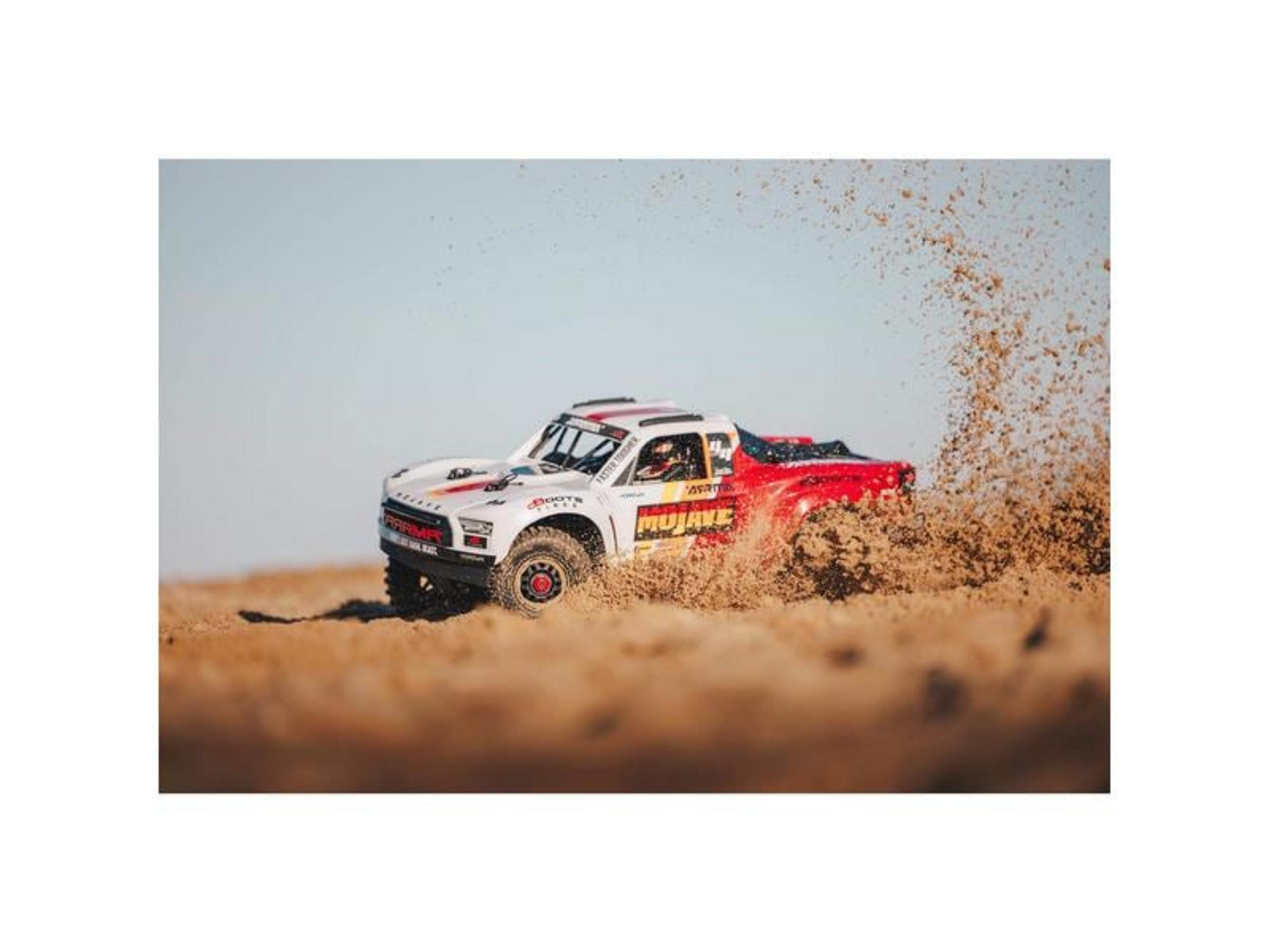Ein weißer und roter ferngesteuerter Truck wirbelt Sand auf, während er auf einer Sandbahn fährt.
