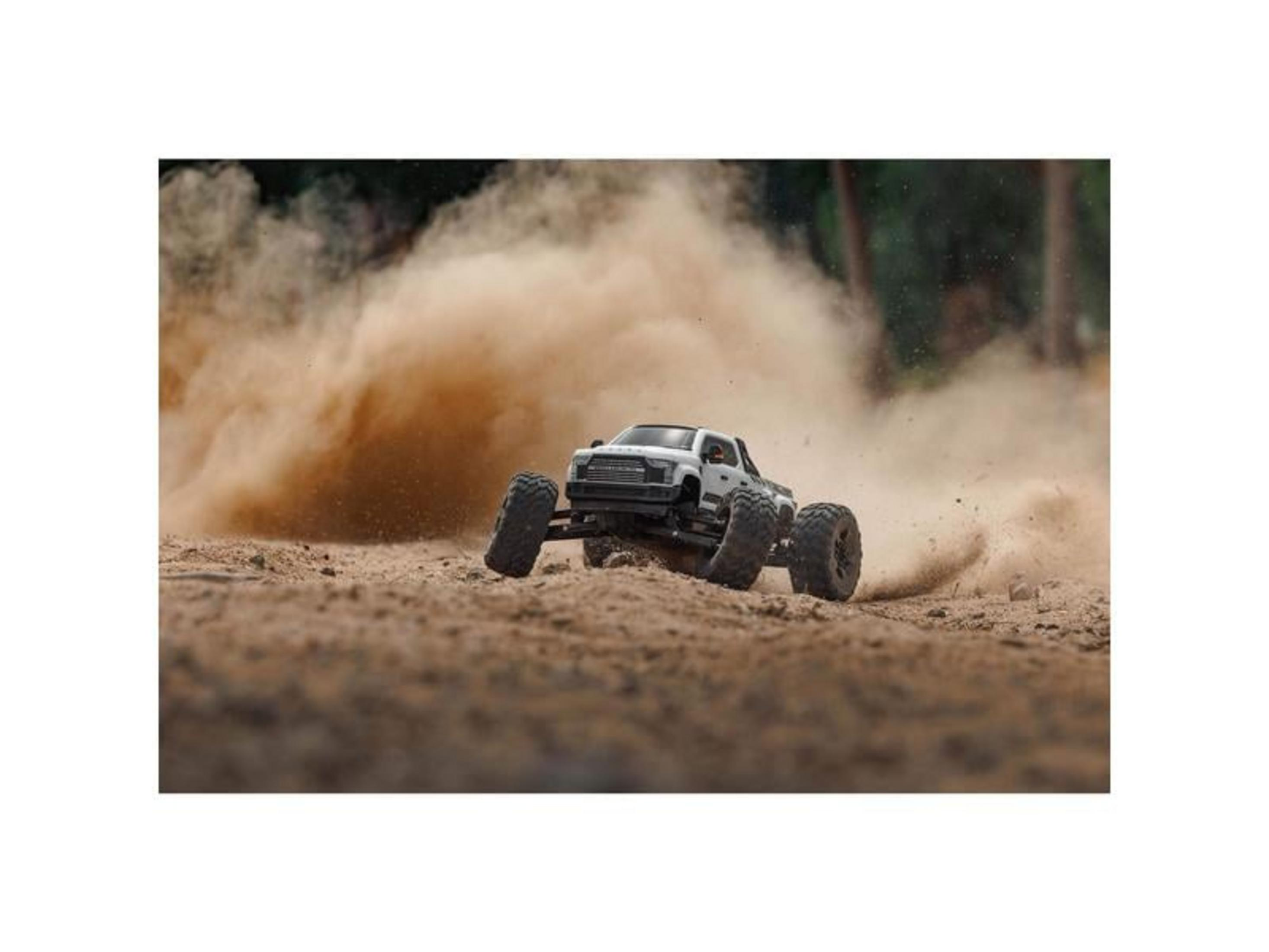 Un coche RC blanco acelera levantando polvo y tierra.