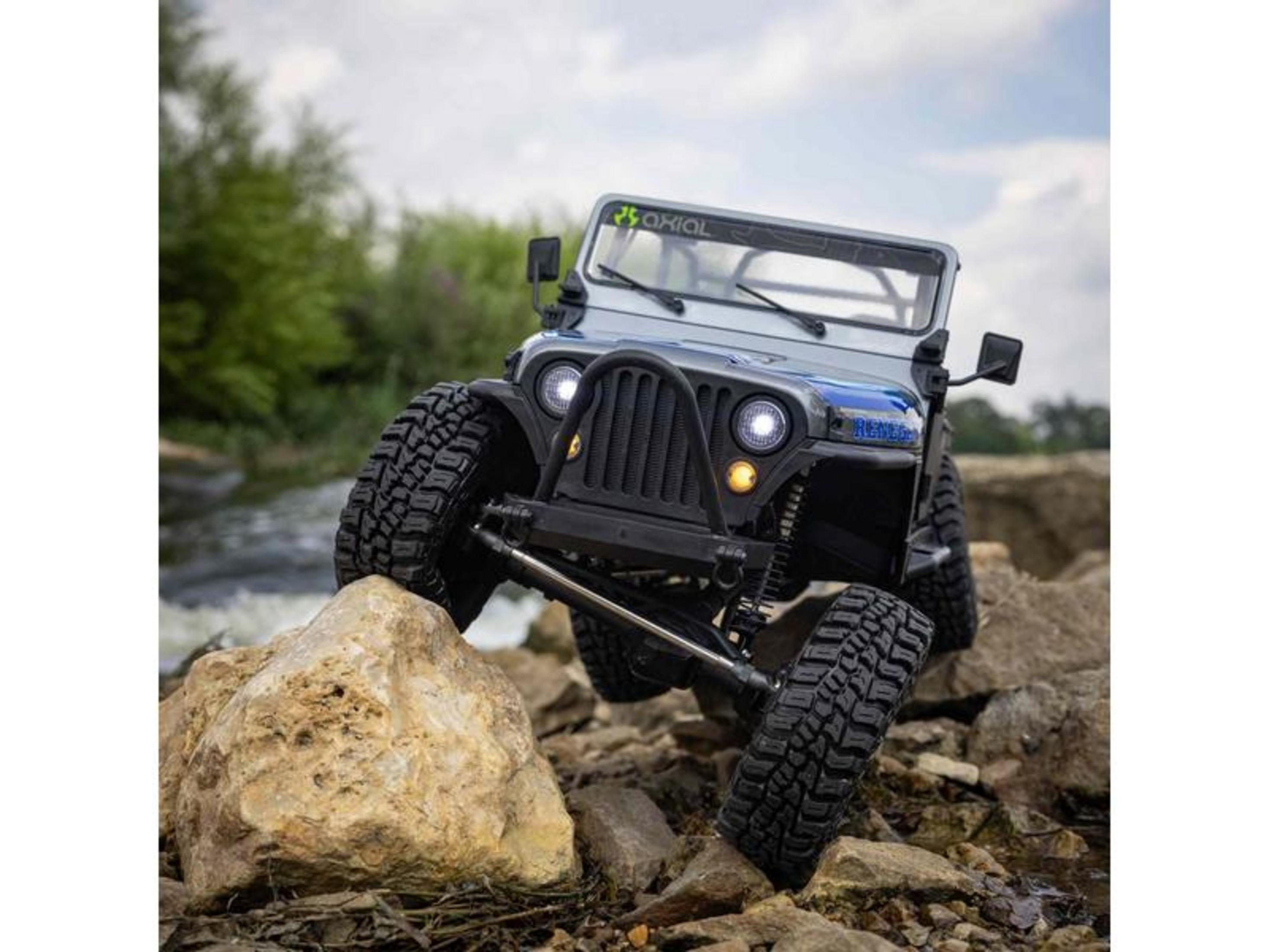 Ein graues RC-Jeep-Modell fährt über Steine in der Nähe eines Flusses.