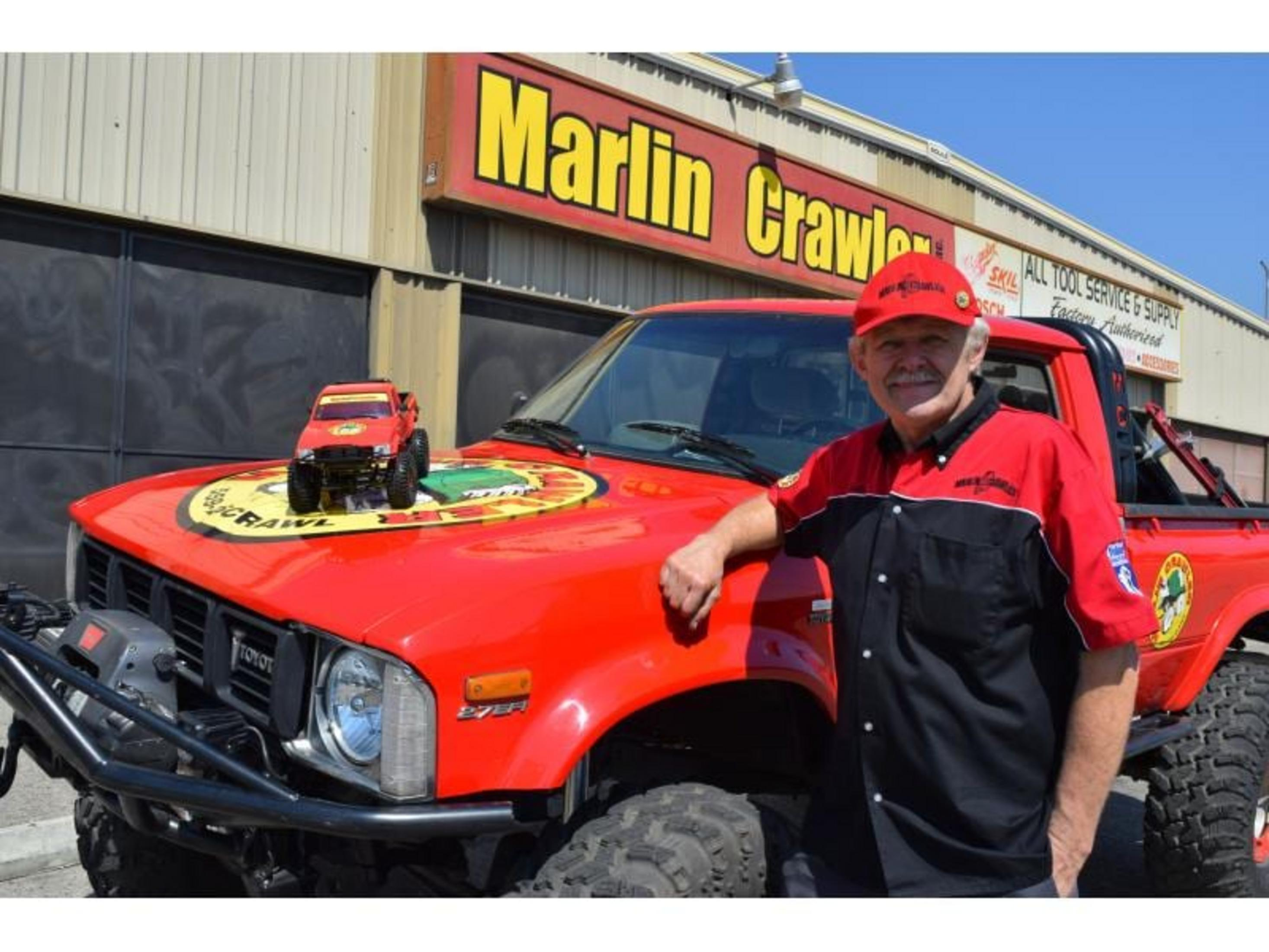 Homme casquette rouge et chemise travail à côté de camion tout-terrain rouge avec jouet sur capot.