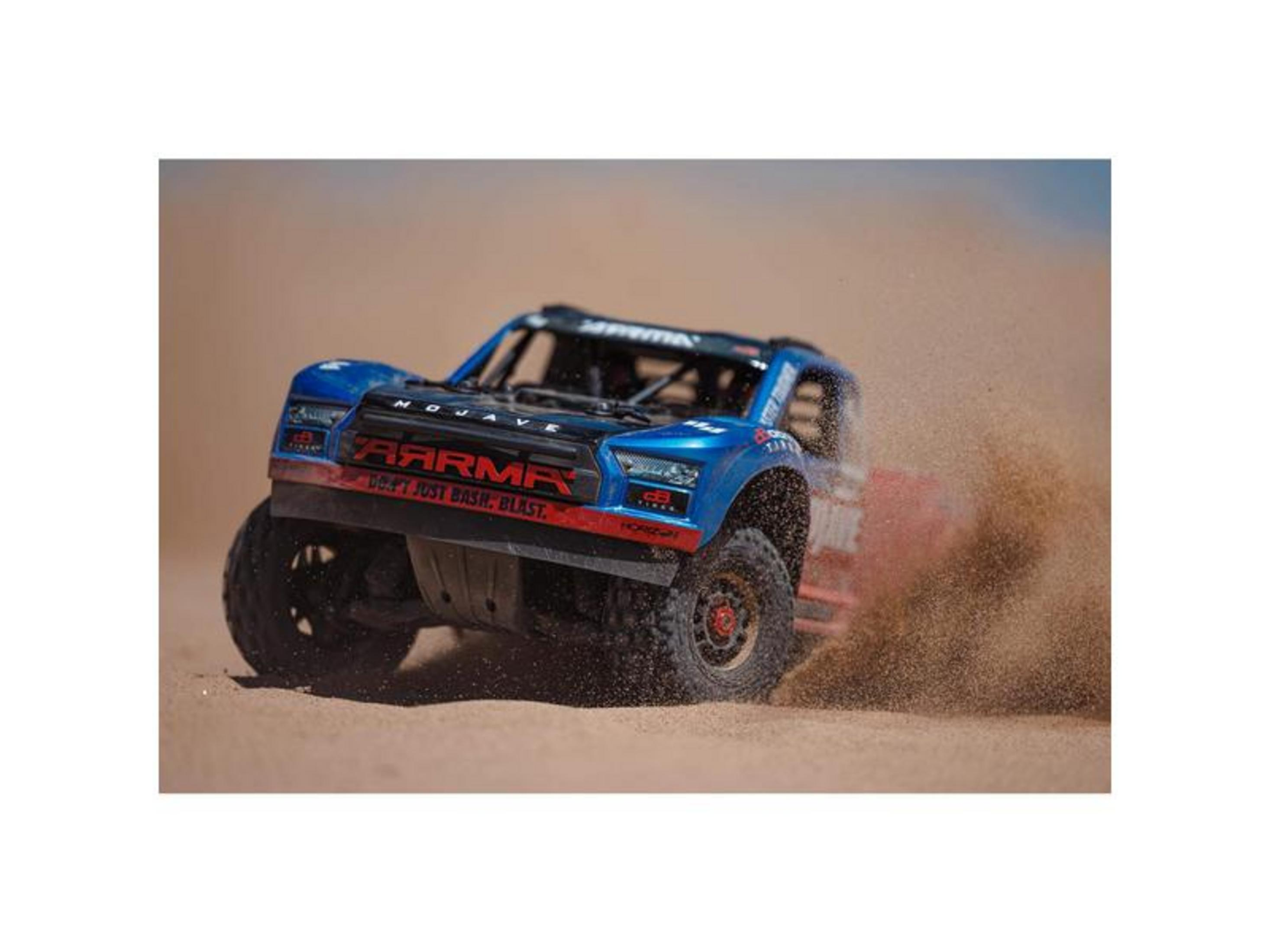 Ein blauer ferngesteuerter Monstertruck fährt schnell über Sand und wirbelt Staub auf.