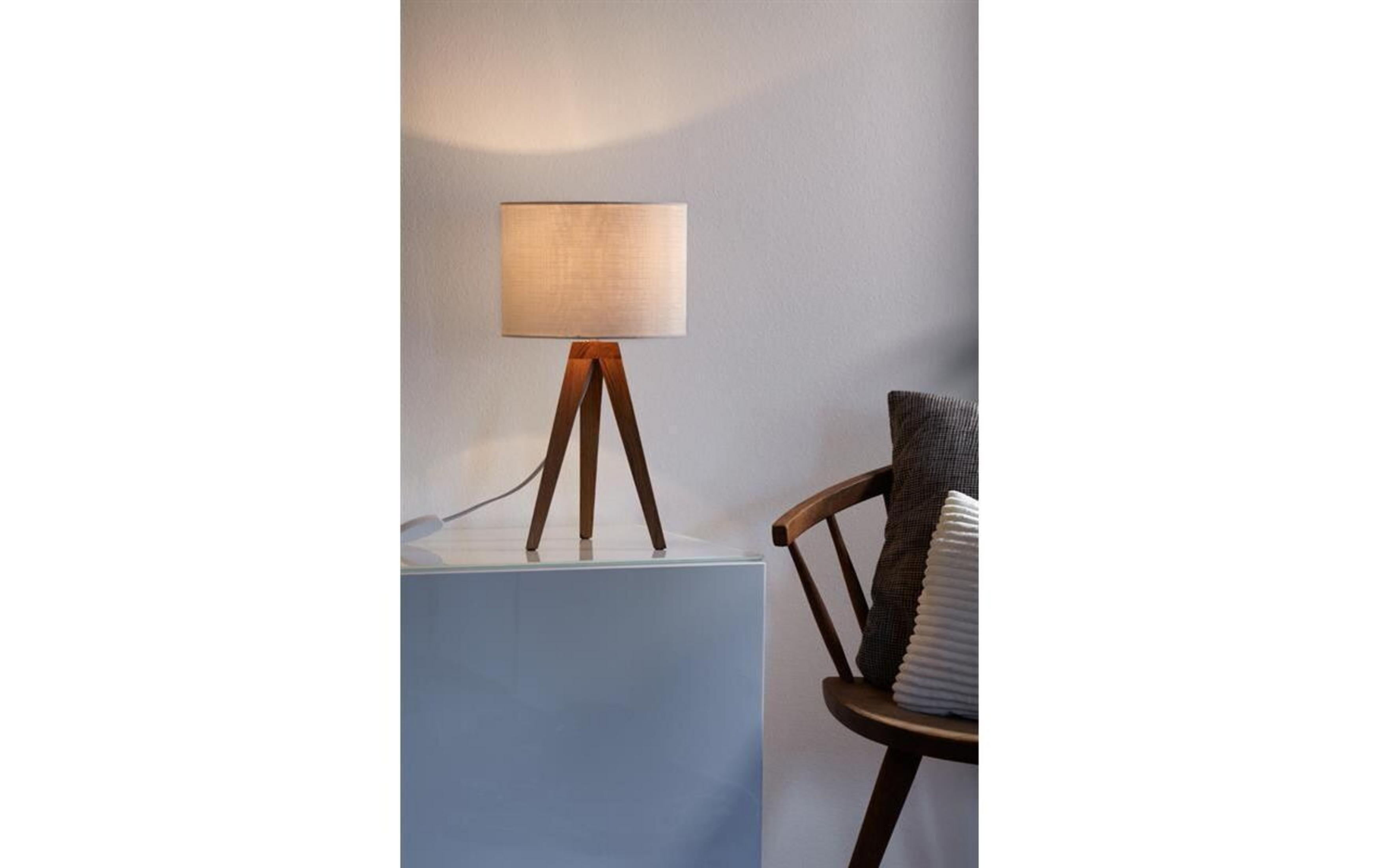 Una lampada con base a treppiede in legno si trova su un tavolo accanto a una sedia con cuscini.