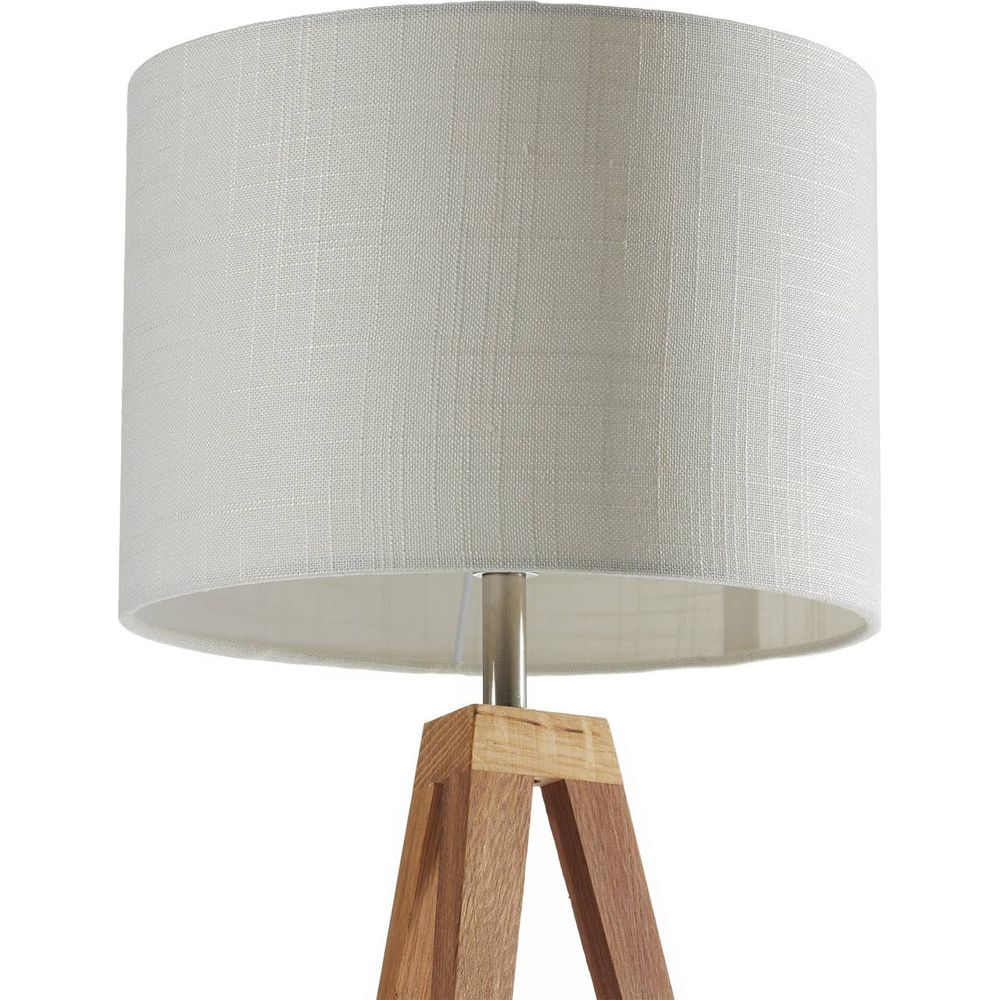 Lampada da terra con paralume bianco e base a treppiede in legno. Primo piano.