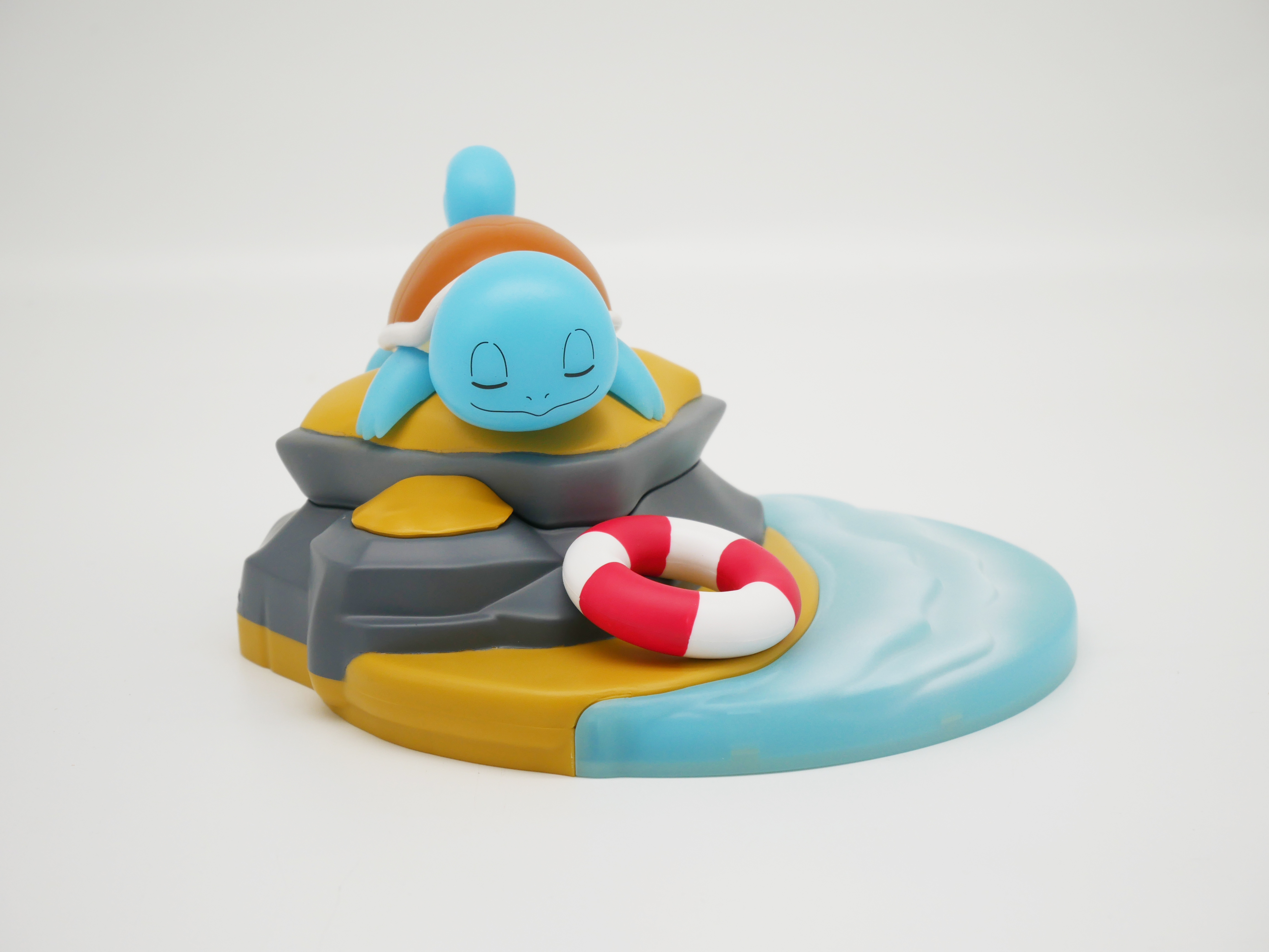 Eine blaue Schildkrötenfigur schläft auf einem Felsen neben einem Rettungsring und Wasser.