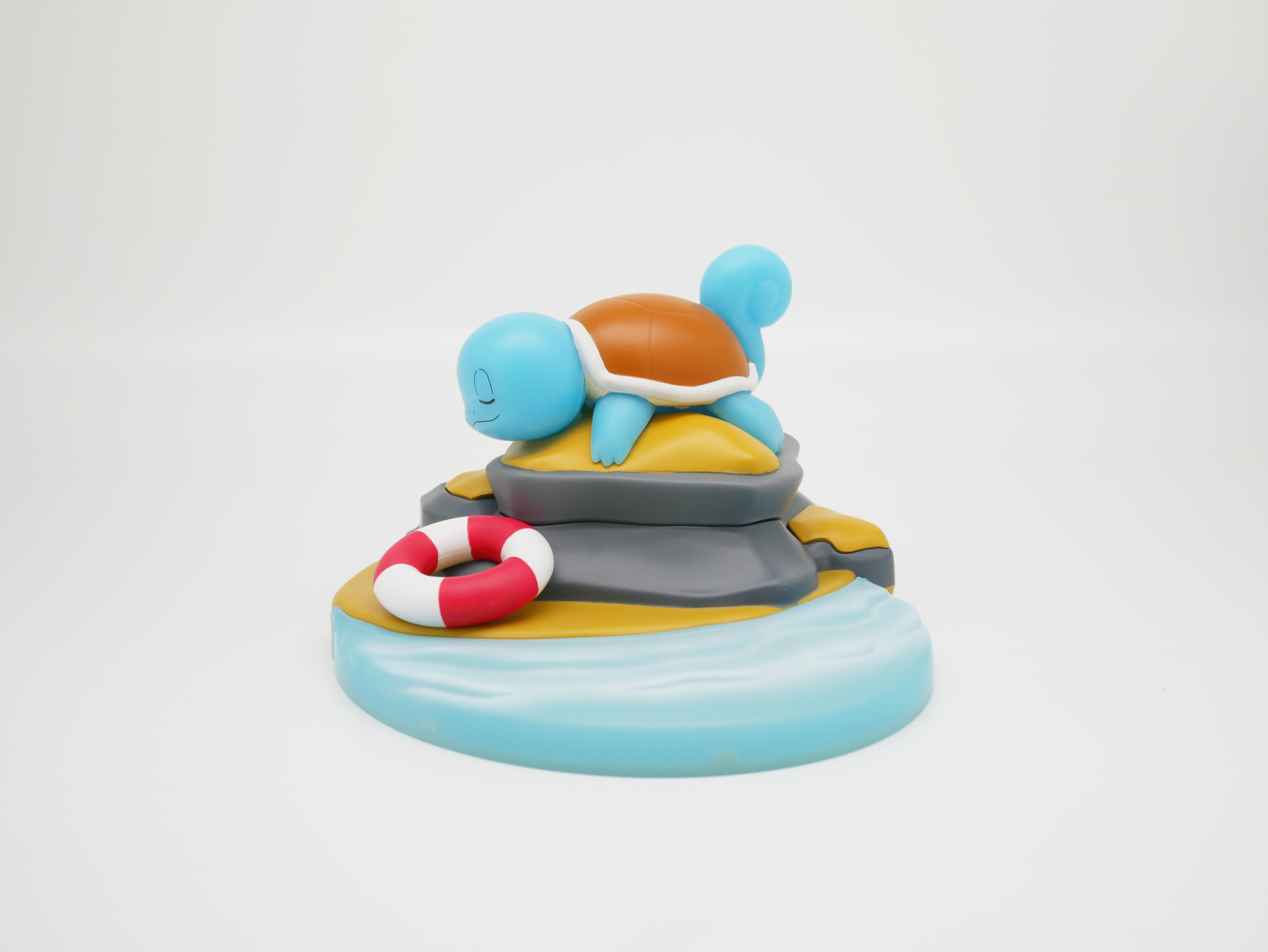 Ein Squirtle-Spielzeug auf einem Felsen mit einem Rettungsring und Wasser.