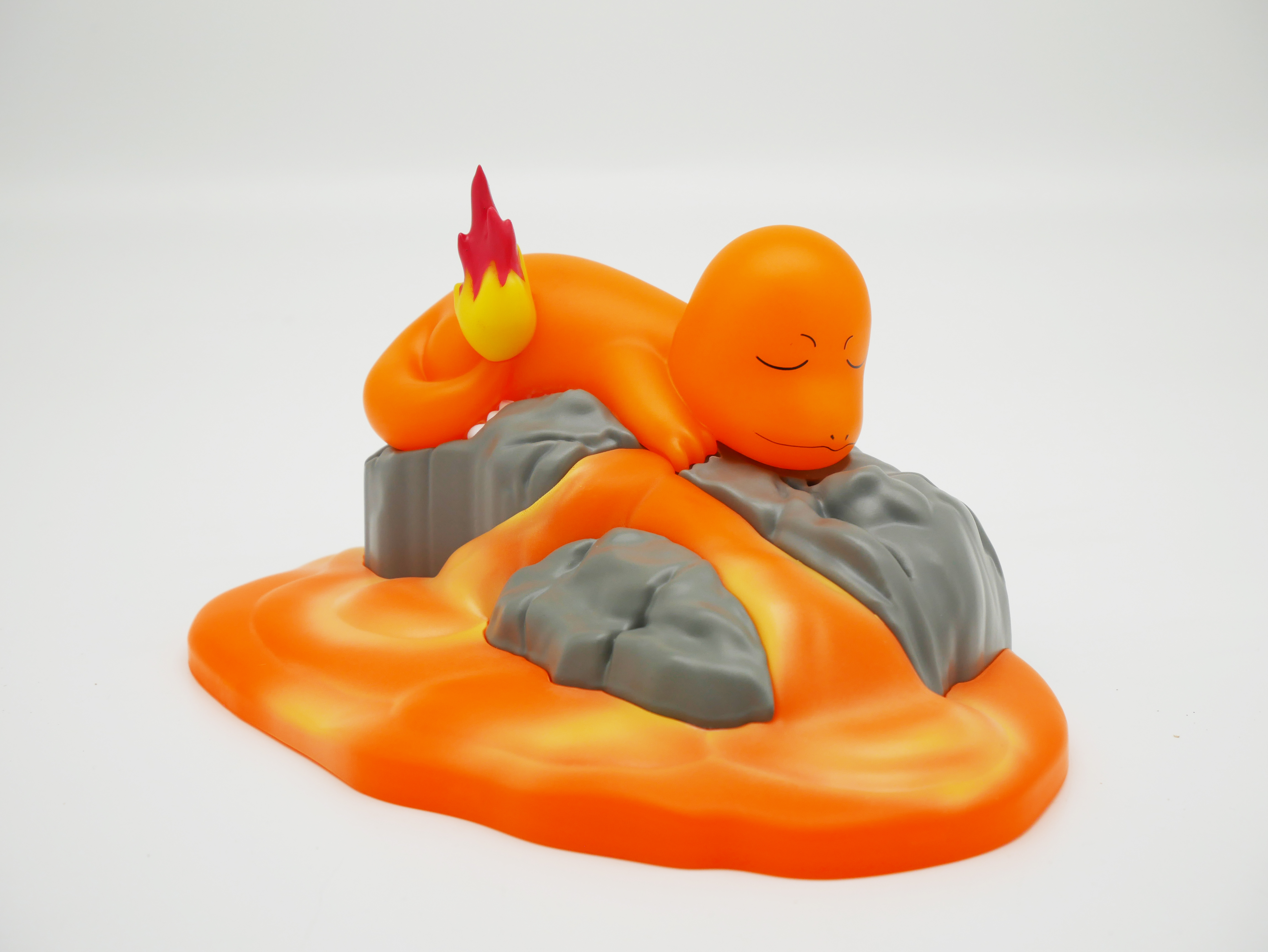 Ein orangefarbener Pokémon-Charakter mit geschlossenen Augen ruht auf grauen Felsen über einer Lava-Umgebung.