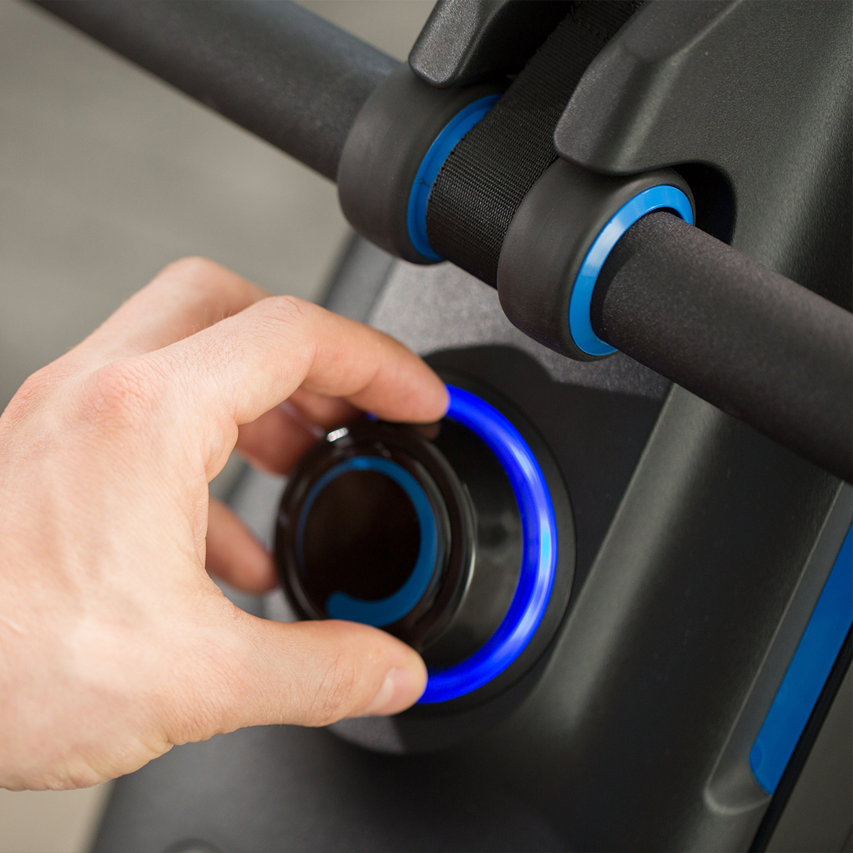 Eine Hand dreht einen schwarzen Knopf mit blauen Ringen auf einem Fitnessgerät.
